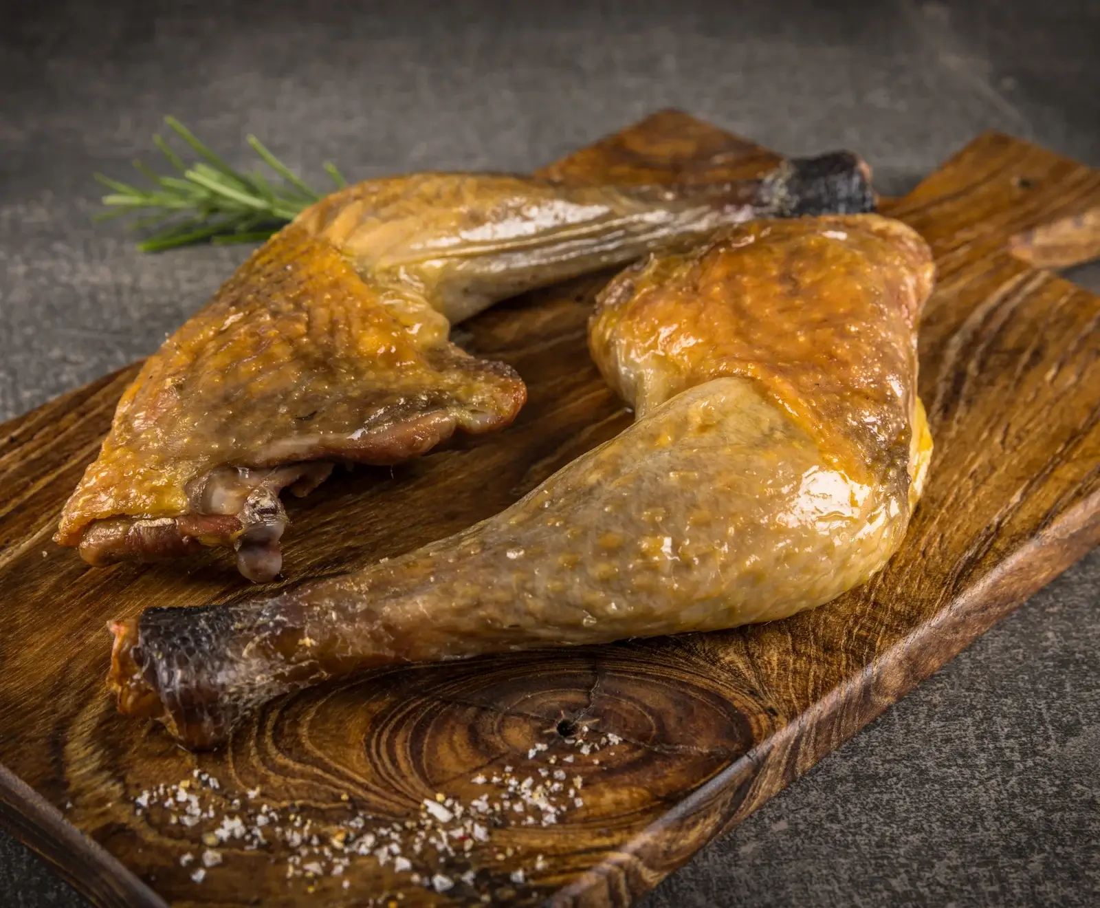 Zwei goldbraun gebratene Hähnchenschenkel auf einem rustikalen Holzbrett, garniert mit einem Rosmarinzweig und grobem Salz.