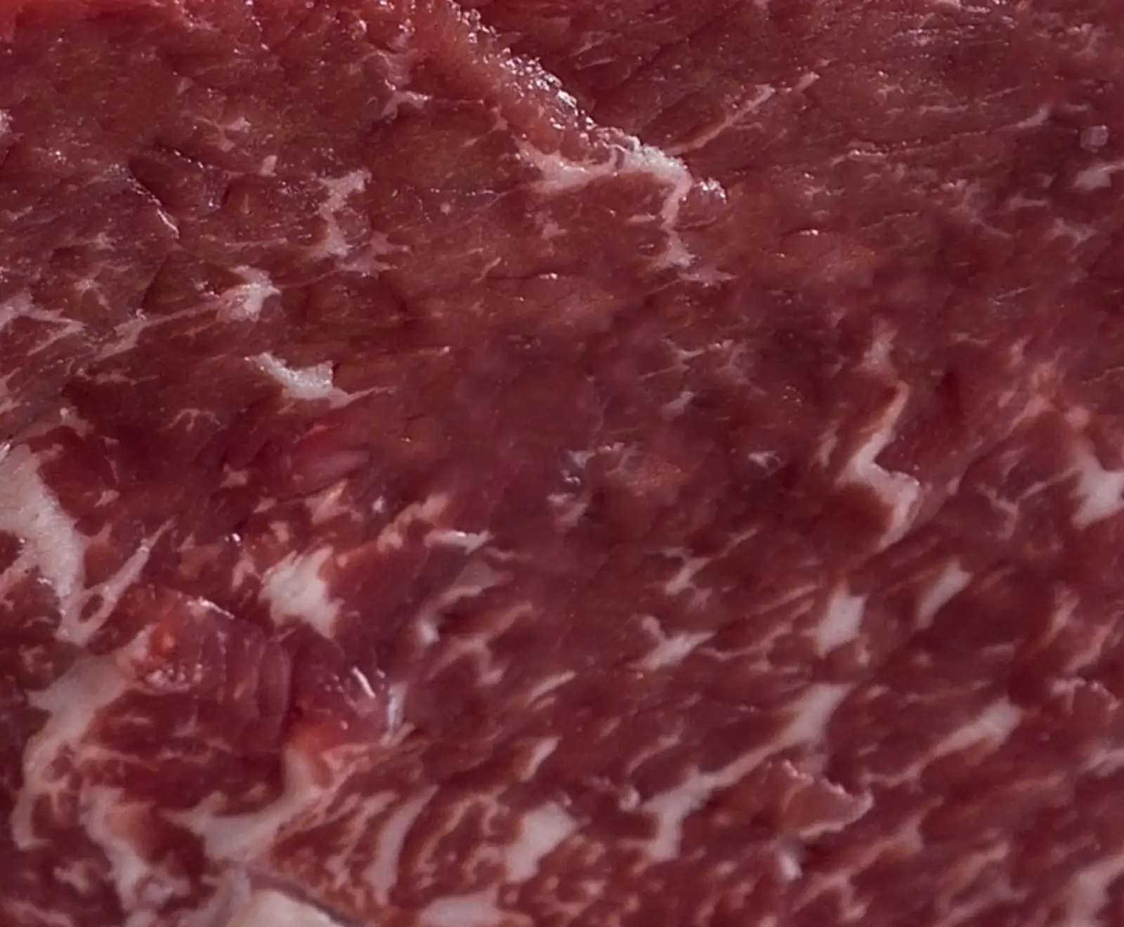 Nahaufnahme von rohem, dunkelrotem Fleisch mit Fettmarmorierung und rauer Oberflächenstruktur