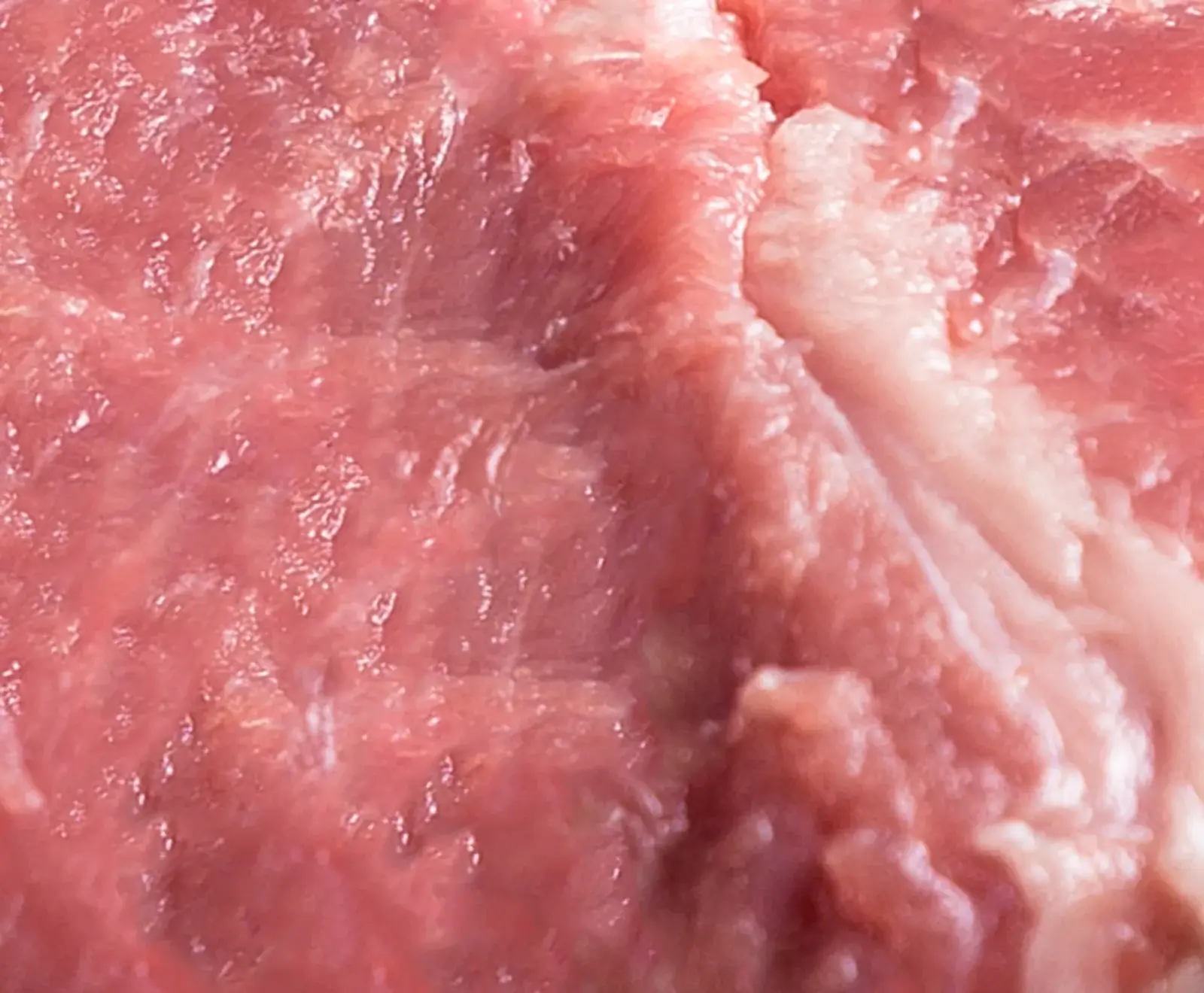 Nahaufnahme von rohem, rötlich-rosa Fleisch mit sichtbaren Muskelfasern und helleren, weißlichen Fett- oder Bindegewebsanteilen. Die Oberfläche ist feucht und strukturiert.