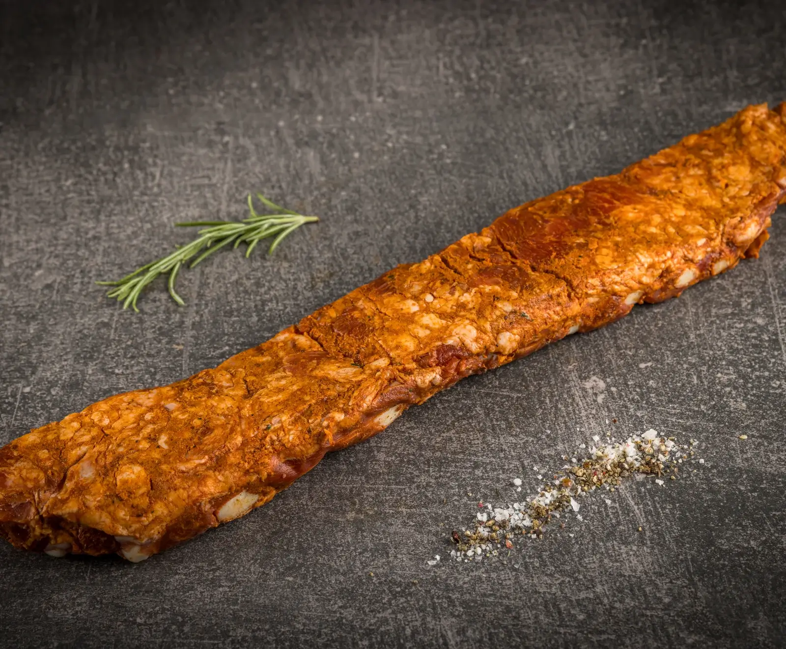 Gebratene Schweinelende mit Kräutern garniert auf dunklem Hintergrund mit Salzkristallen daneben.