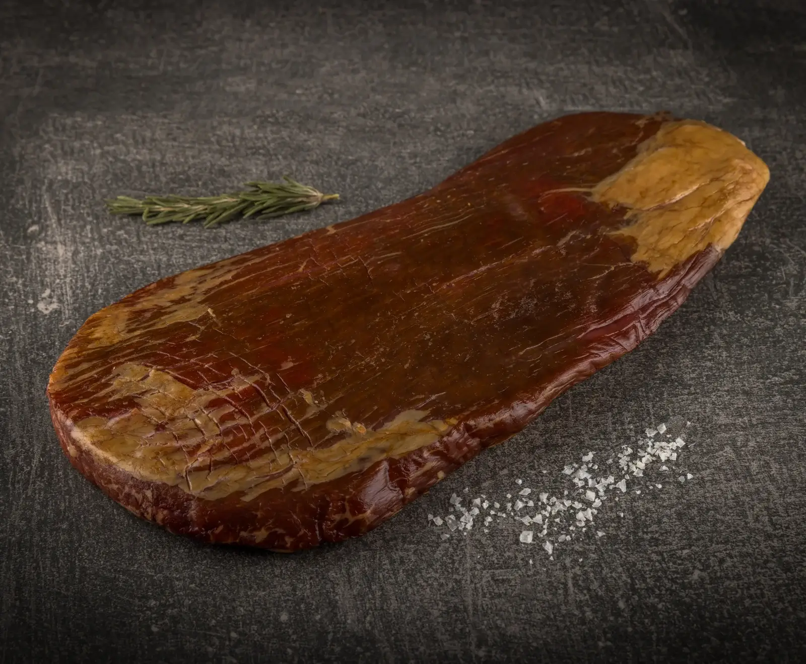 Ein Stück rohes Rindfleisch mit Rosmarin garniert und Salz bestreut auf dunklem Hintergrund.