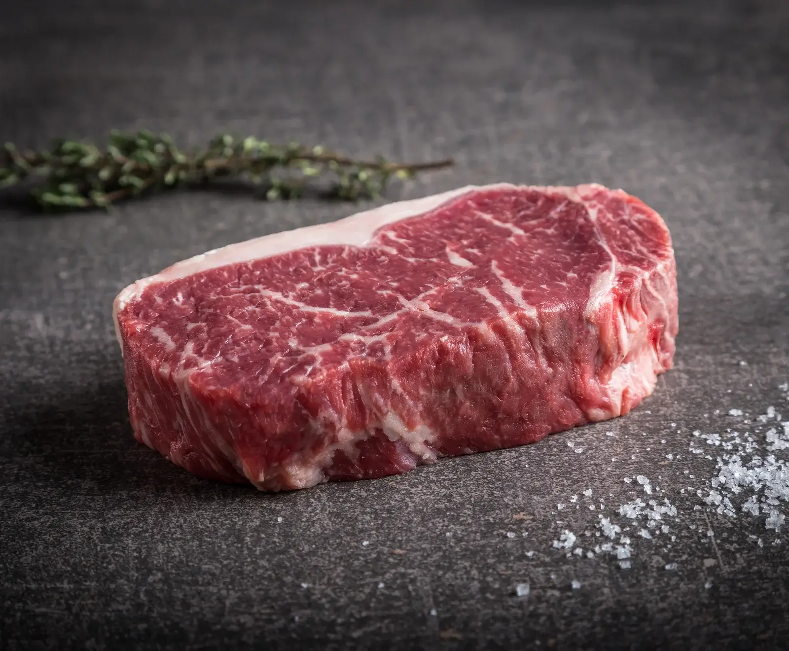 Rohes Rinderfilet-Steak mit Salz bestreut, auf dunklem Hintergrund mit grünen Pflanzenteilen im Hintergrund.