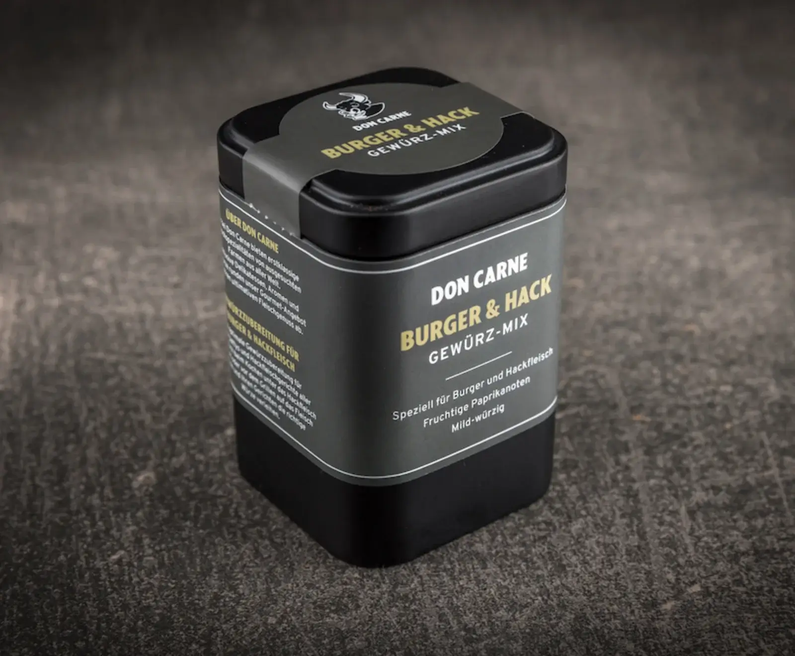 Schwarze, quadratische Gewürzdose von Don Carne mit gold-schwarzem Etikett für Burger & Hack Gewürz-Mix, das fruchtige Paprikanoten und mild-würzigen Geschmack verspricht, auf dunklem Untergrund.