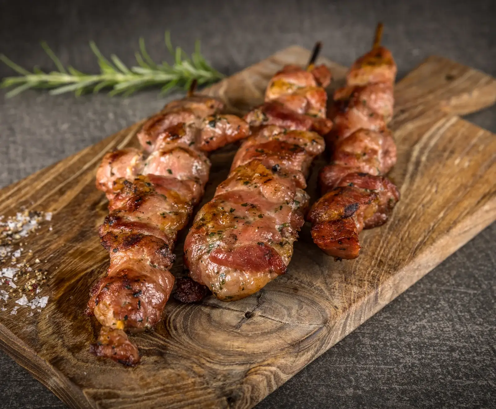 Mehrere gegrillte Schweinefilet-Spieße mit Kräutern auf einem Holzbrett serviert.