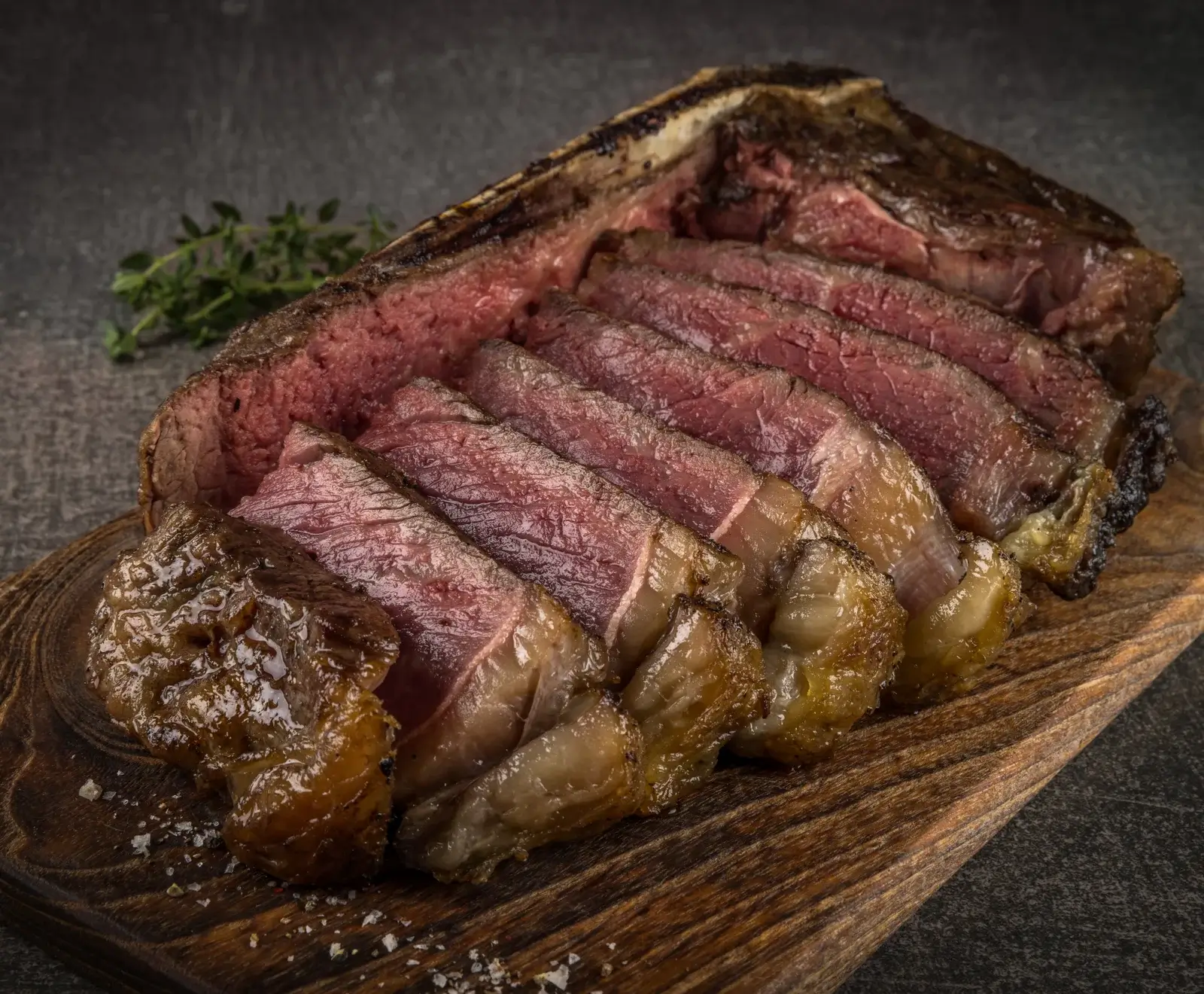 Nahaufnahme eines perfekt gegarten, aufgeschnittenen T-Bone Steaks mit rosa Kern und knuspriger Kruste, serviert auf einem rustikalen Holzbrett mit Meersalz und Thymianzweig.