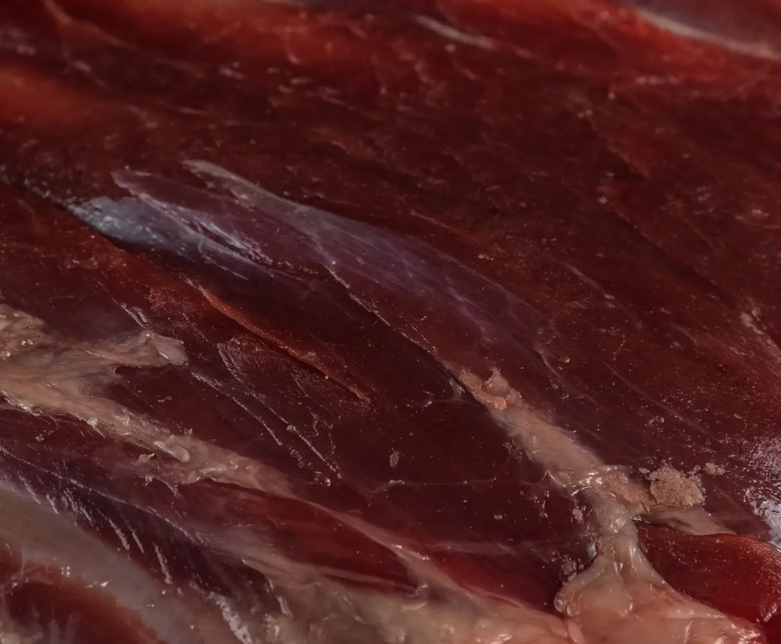 Nahaufnahme von dunkelrotem, rohem Fleisch mit deutlich sichtbaren Muskelfasern und helleren, glänzenden Bindegewebsstreifen.