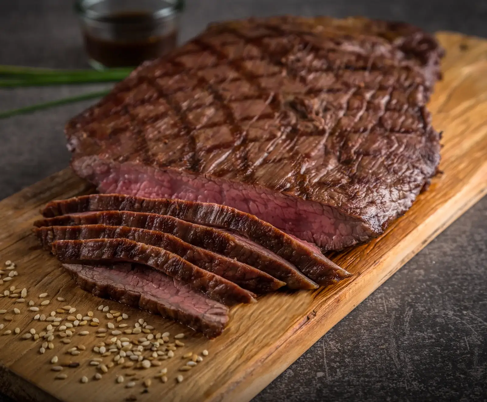 Gegrilltes Flanksteak, in dünne Scheiben geschnitten, mit Sesamsamen auf einem Holzbrett serviert