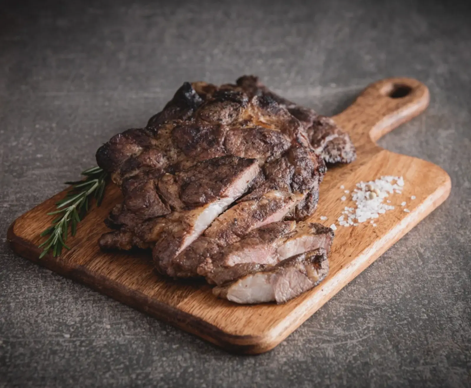 Geschnittenes, gegrilltes Steak auf einem Holzbrett, garniert mit einem Rosmarinzweig und Salz