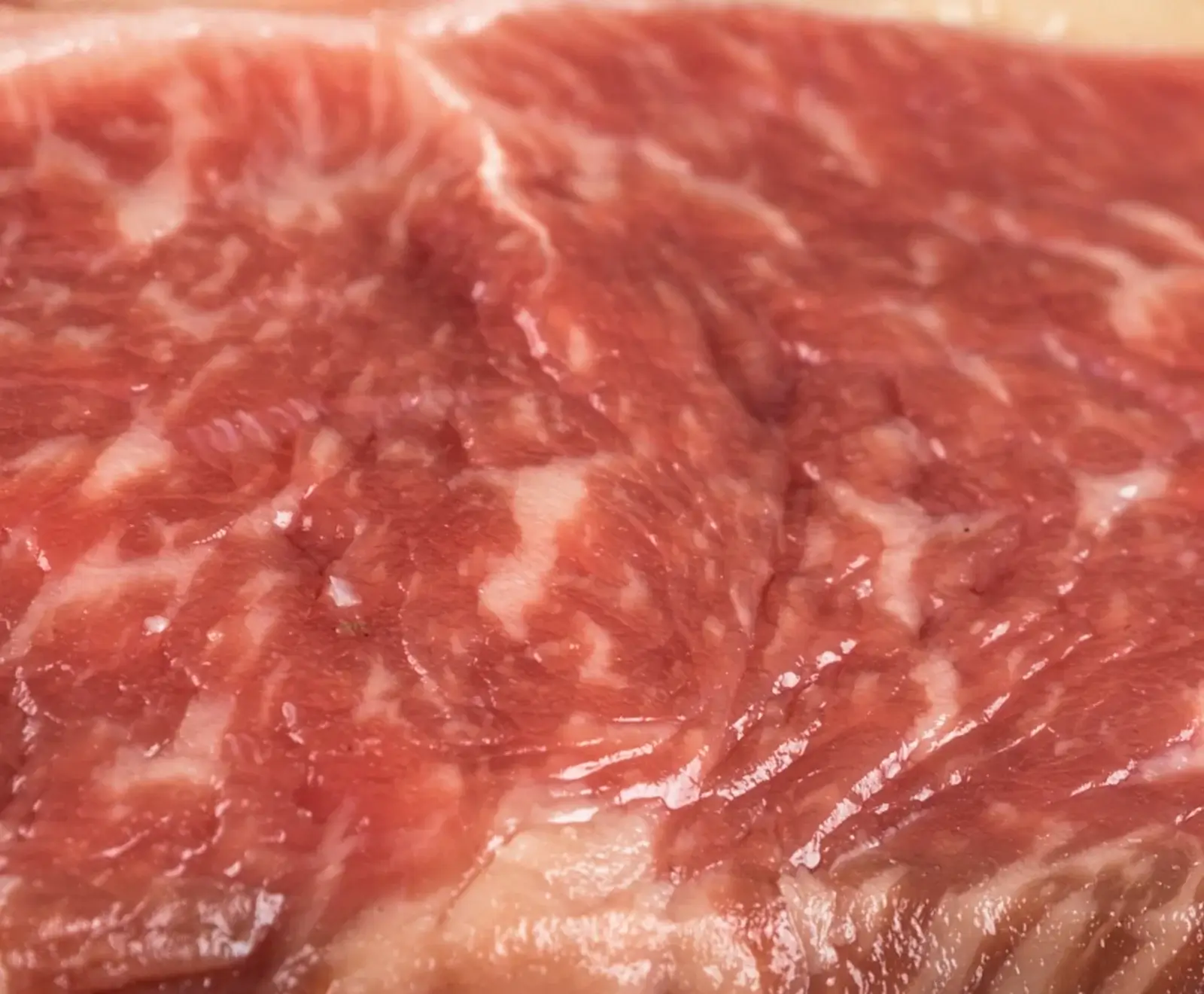 Nahaufnahme von rohem, stark marmoriertem Rindfleisch mit roten Muskelfasern und weißen Fettadern. Die Oberfläche glänzt leicht.