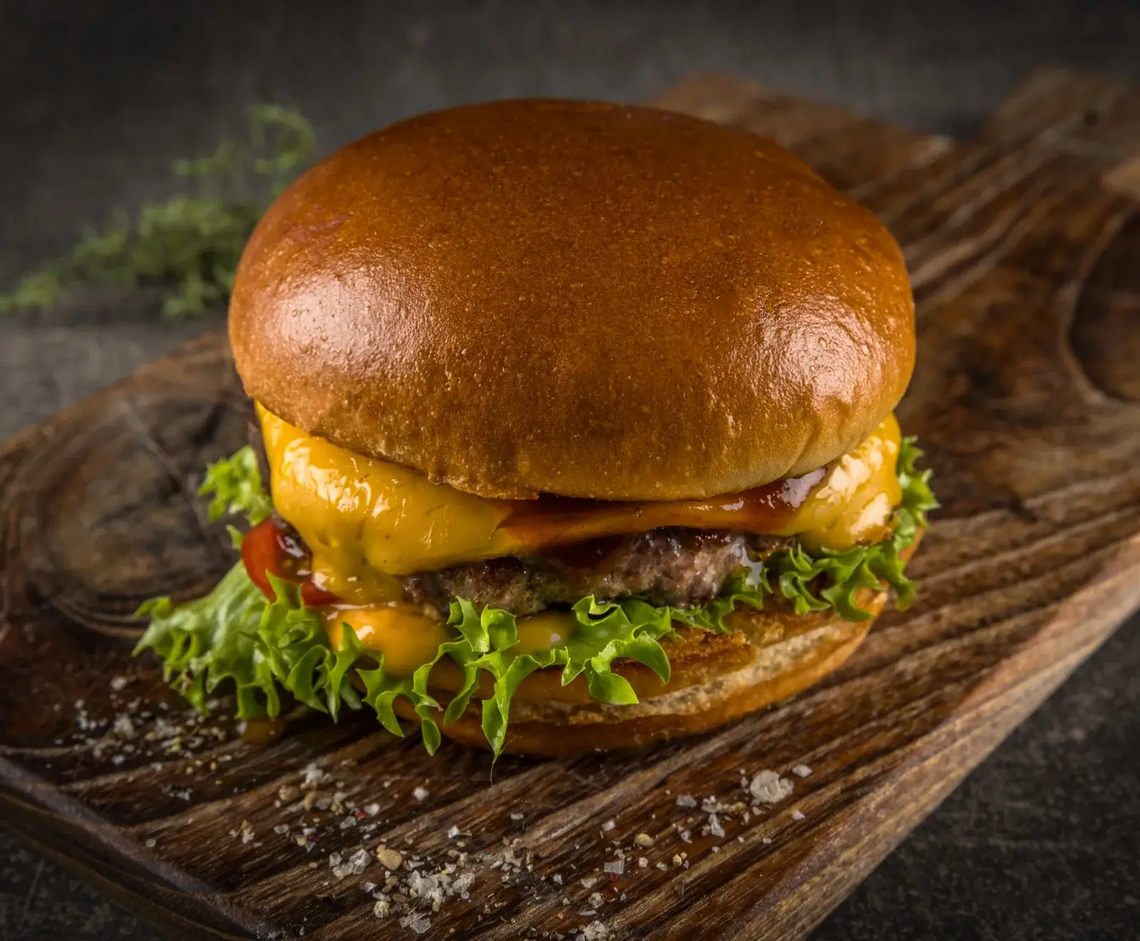 Ein appetitlicher Gourmet-Cheeseburger mit goldbraunem Brötchen, saftigem Rindfleisch-Patty, geschmolzenem Käse, frischem Salat und Soße, serviert auf einem rustikalen Holzbrett.