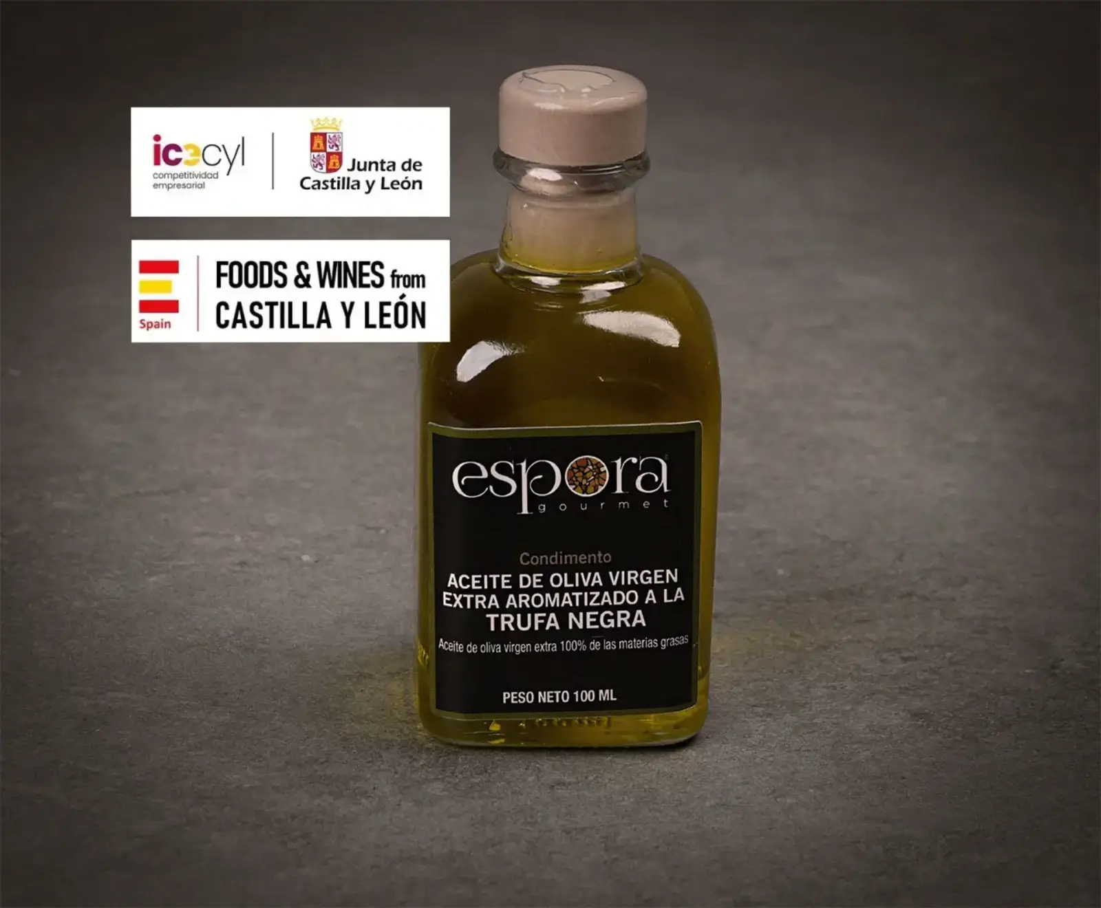 Eine kleine Flasche Espora Gourmet natives Olivenöl extra mit schwarzem Trüffelgeschmack (100 ml) auf dunklem Hintergrund. Oben links sind Logos von Castilla y León und "Foods & Wines from Castilla y León" zu sehen.