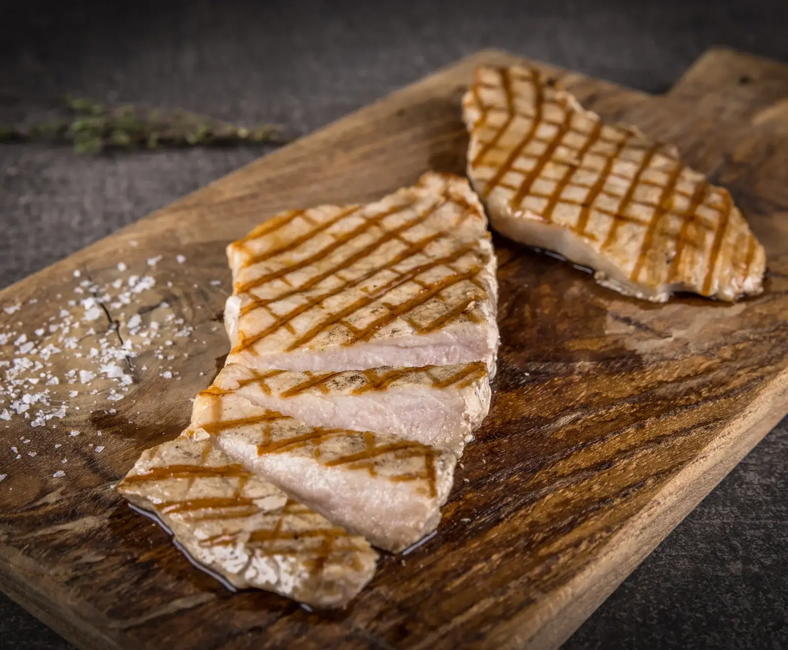 Gegrillte Thunfischsteaks auf einem Holzbrett, garniert mit Salz und Thymian