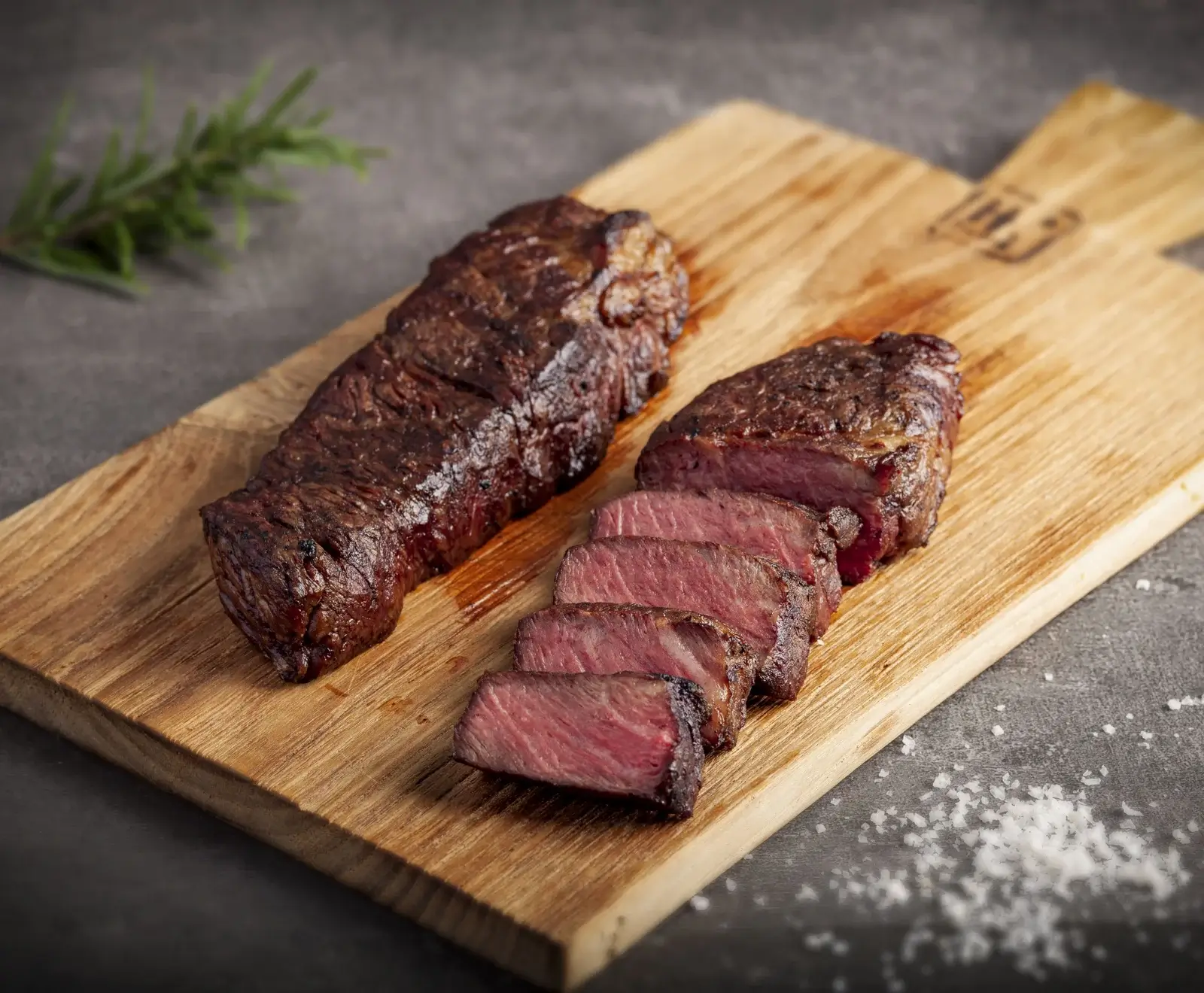 Zwei Scheiben gegrilltes Rinderfilet auf einem Holzbrett, garniert mit Rosmarin und Salz.