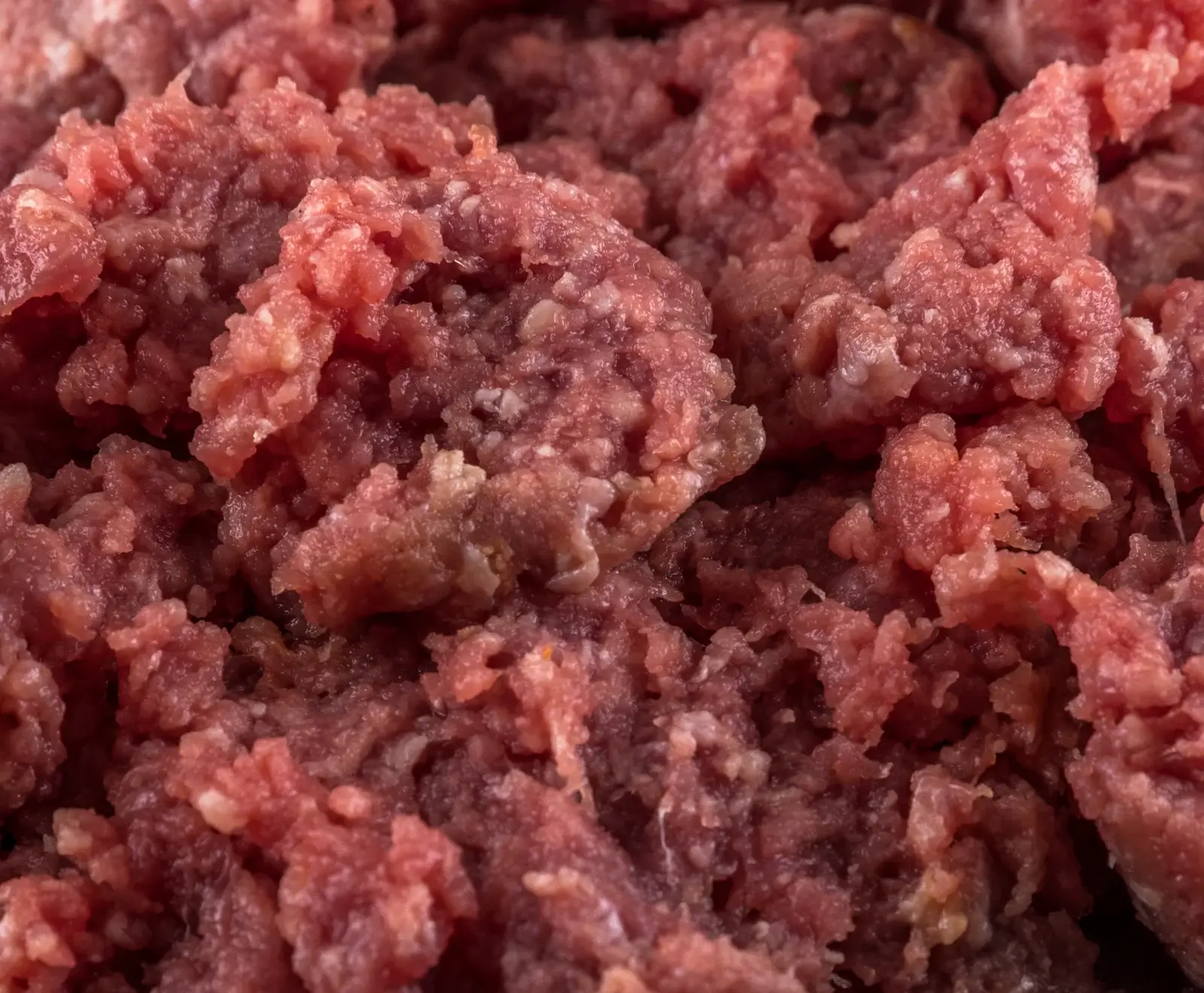 Nahaufnahme von rohem, rötlich-rosa Hackfleisch mit sichtbaren weißen Fettstücken, das eine ungleichmäßige, grobe Textur aufweist.