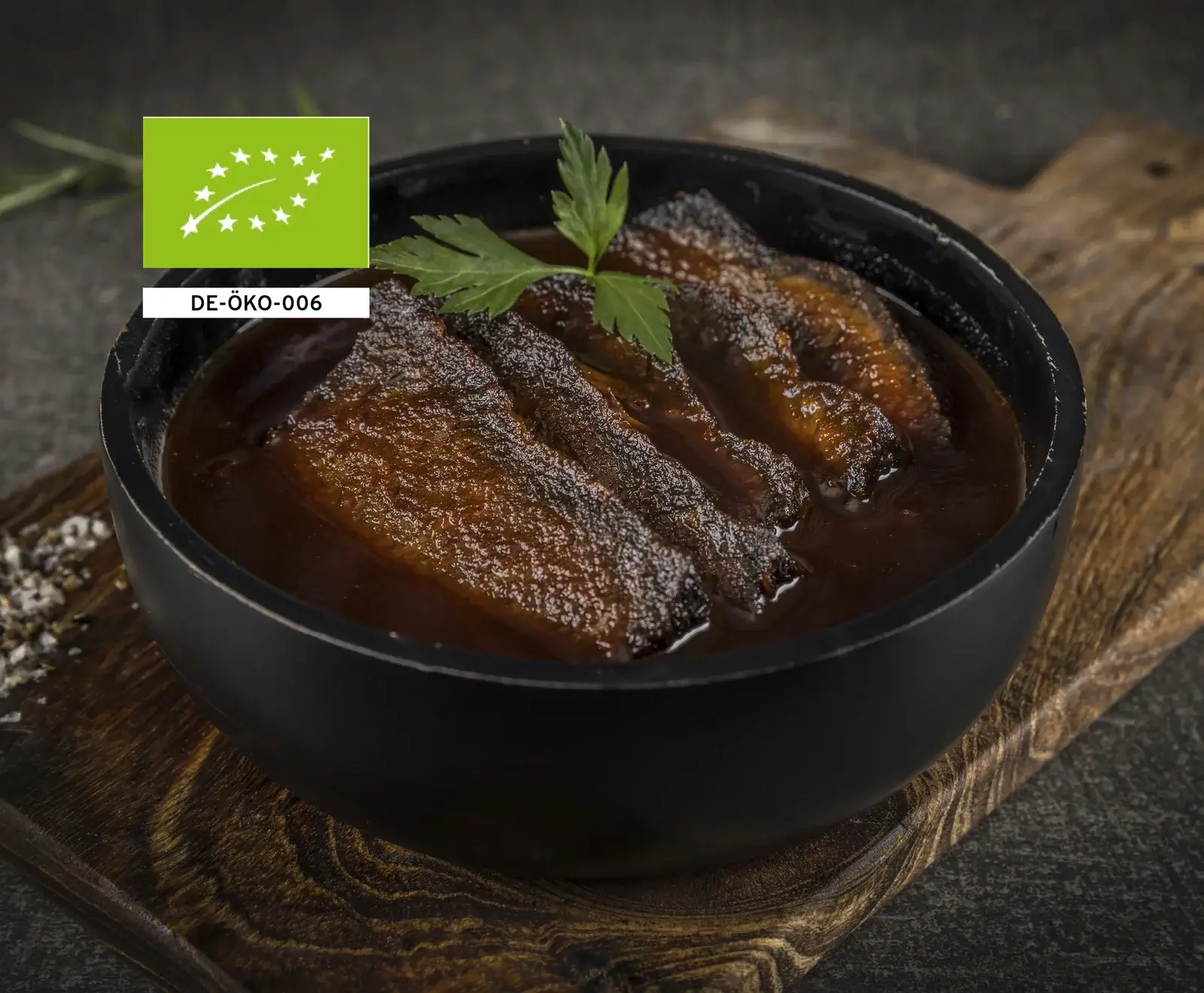 Gegrillte Auberginen in einer schwarzen Schüssel, garniert mit Petersilienblättern, auf einem Holzbrett.