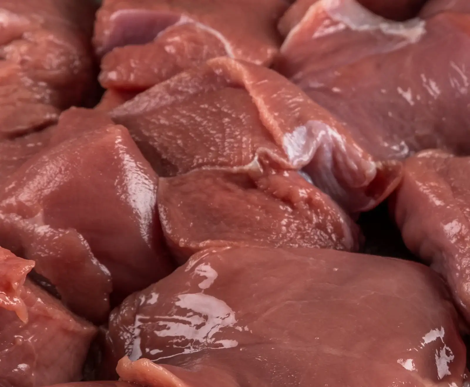 Nahaufnahme von vielen rohen, rötlich-rosa Fleischstücken, die dicht beieinander liegen. Das magere Fleisch ist feucht und glänzend, bereit zur Zubereitung.