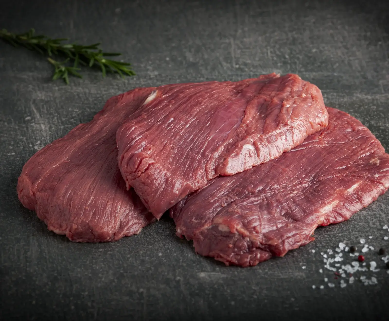 Zwei rohe Rindersteaks mit Rosmarin auf einer dunklen Schieferoberfläche mit Salz