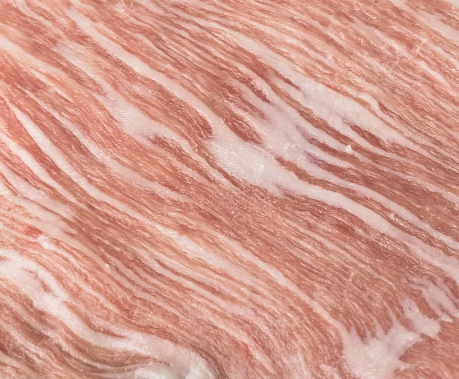 Nahaufnahme von rohem, dünn geschnittenem Fleisch mit ausgeprägten diagonalen Streifen aus rosa Muskelfleisch und weißem Fett, die eine marmorierte Textur bilden.
