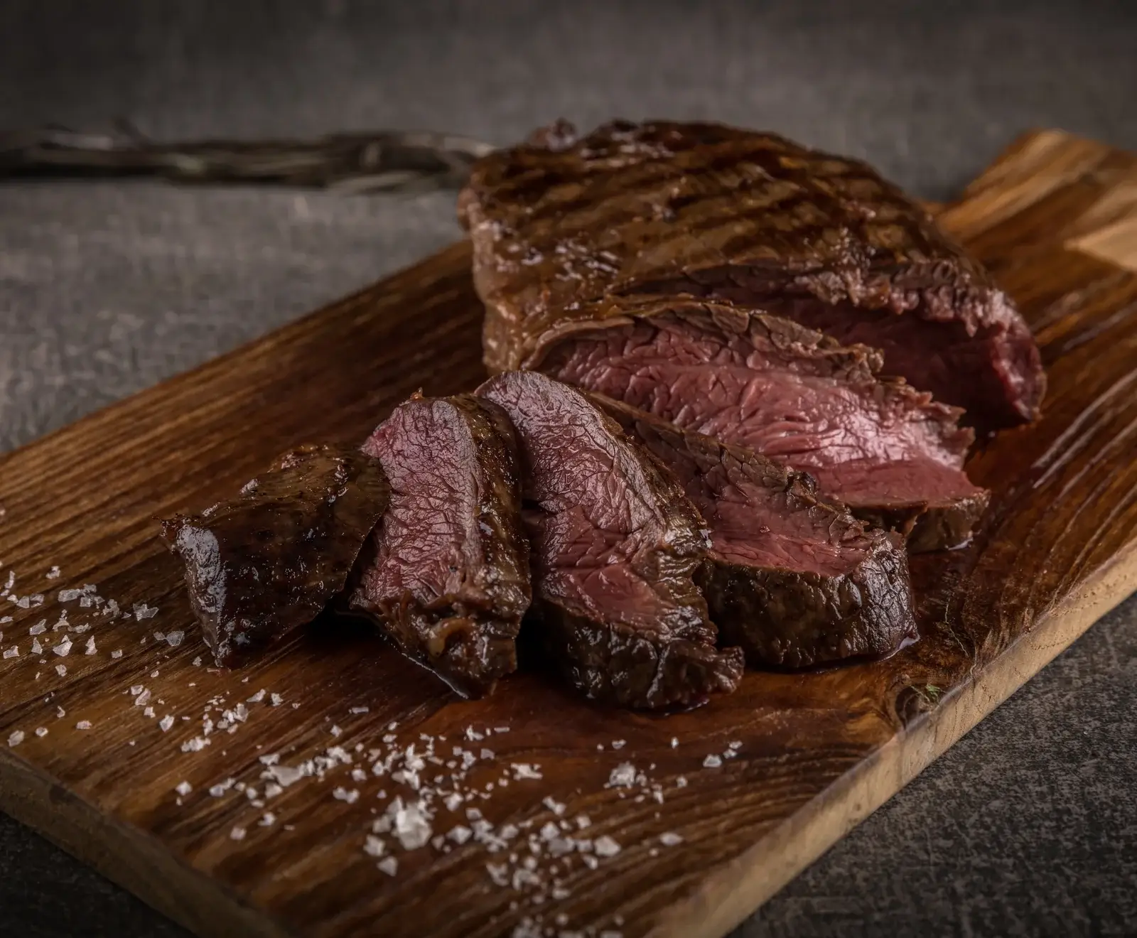 Gegrilltes Steak mit perfekter Kruste, in Scheiben geschnitten und auf Holzbrett serviert, mit Salz bestreut