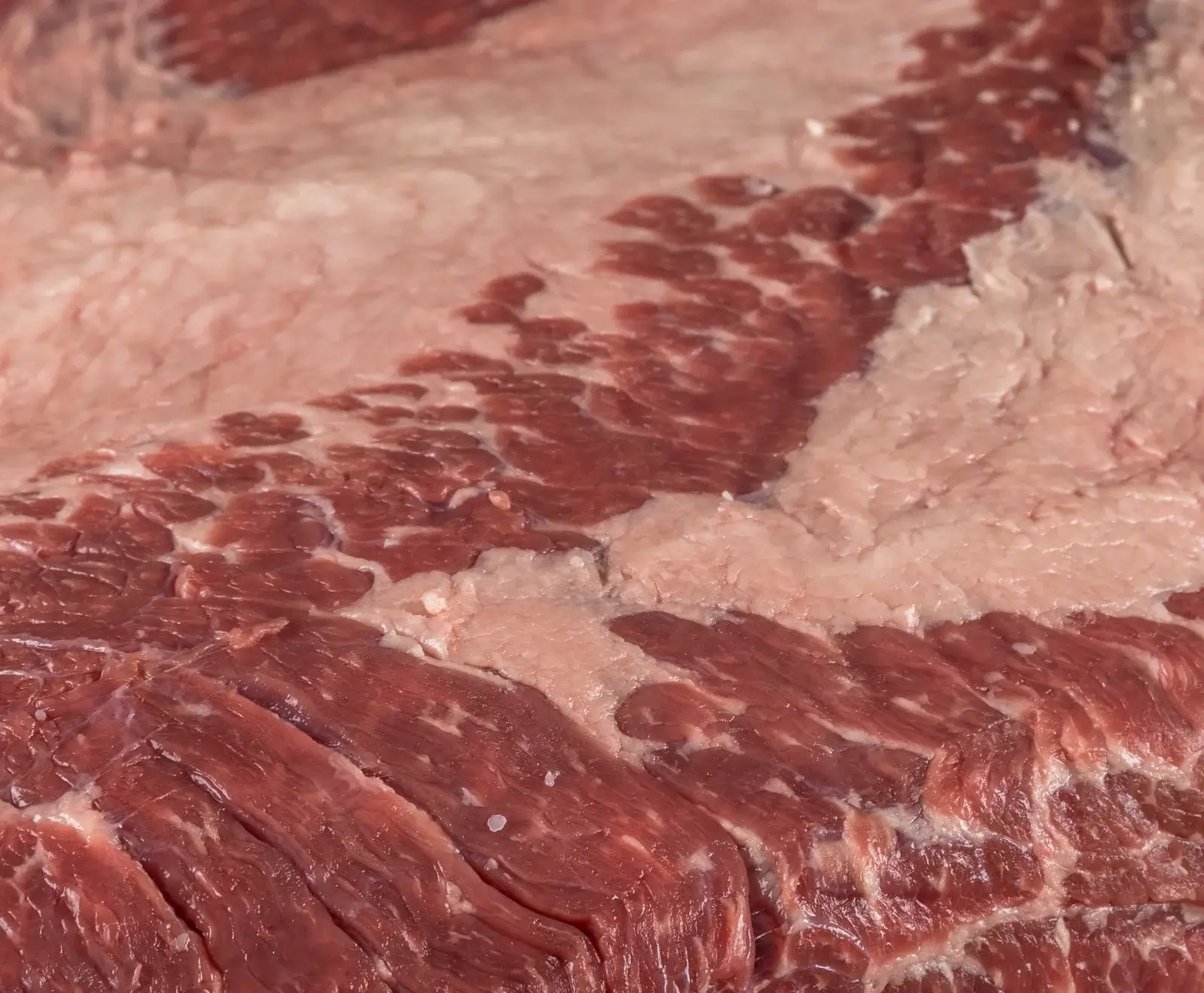 Nahaufnahme von rohem Rindfleisch mit deutlicher Marmorierung aus roten Muskelfasern und weißen Fettadern.
