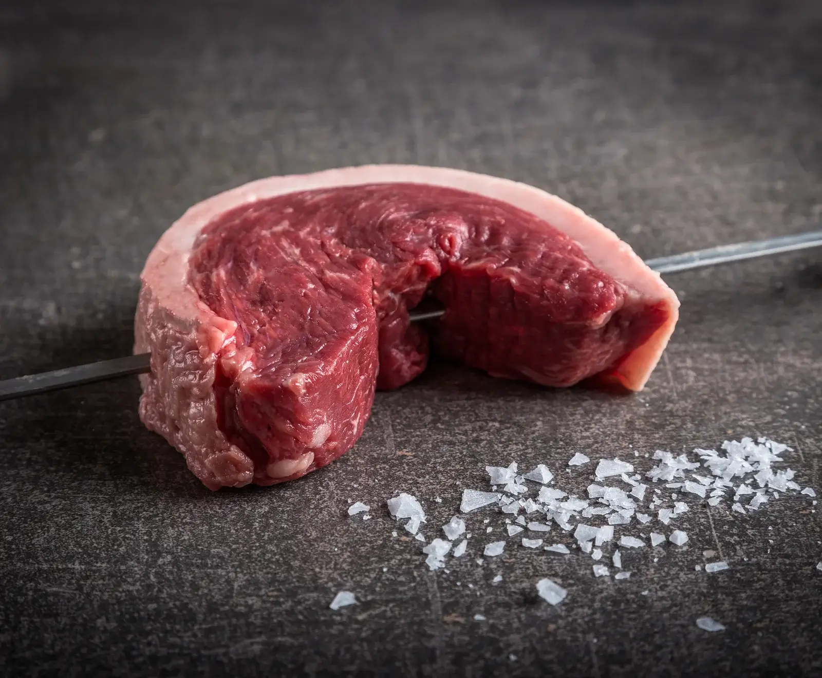 Rohes Rinderfilet auf dunklem Hintergrund mit Salzkristallen daneben