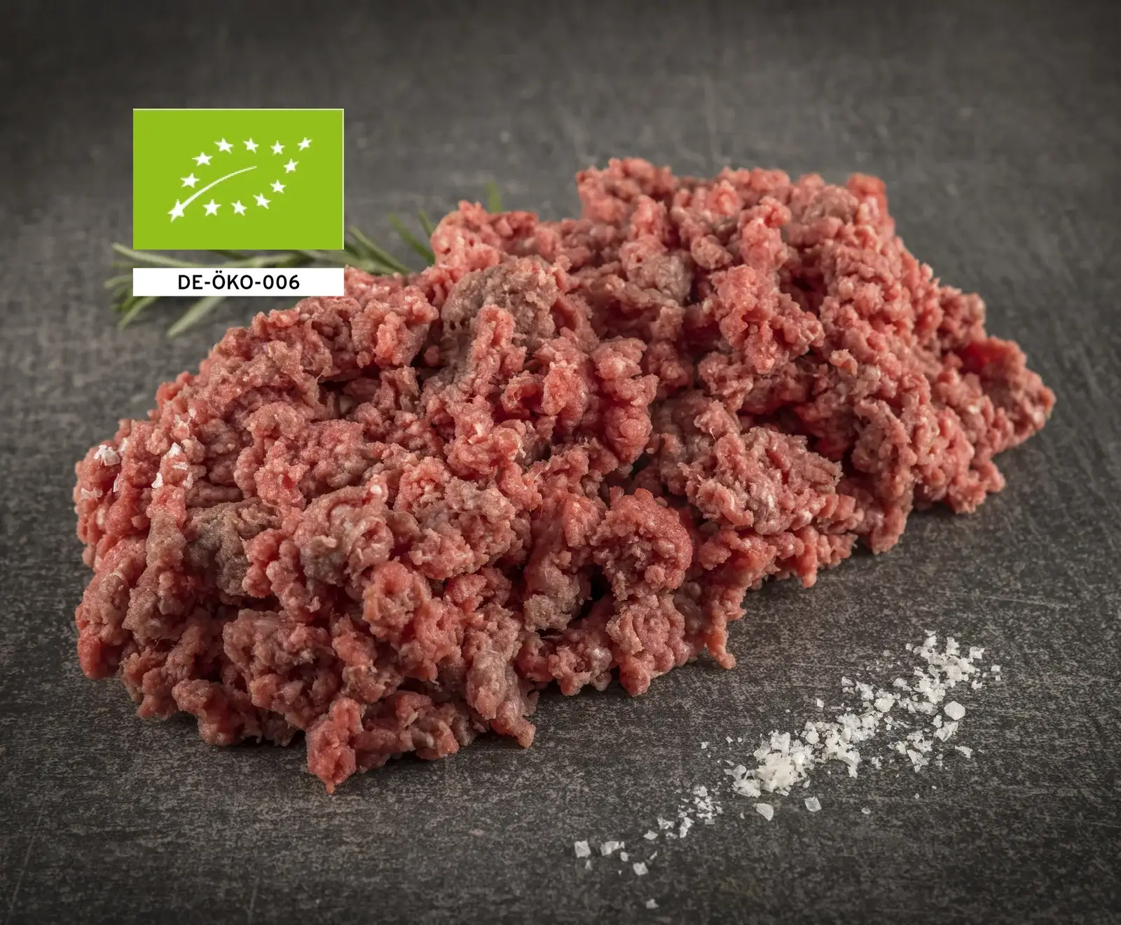 Rohes Bio-Rinderhackfleisch auf dunklem Hintergrund, mit EU-Bio-Siegel und Salz daneben.
