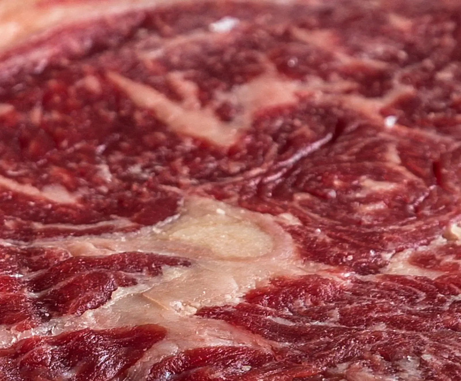 Nahaufnahme von rohem Rindfleisch mit ausgeprägter Marmorierung, die rote Muskelfasern und weiße Fettadern zeigt.
