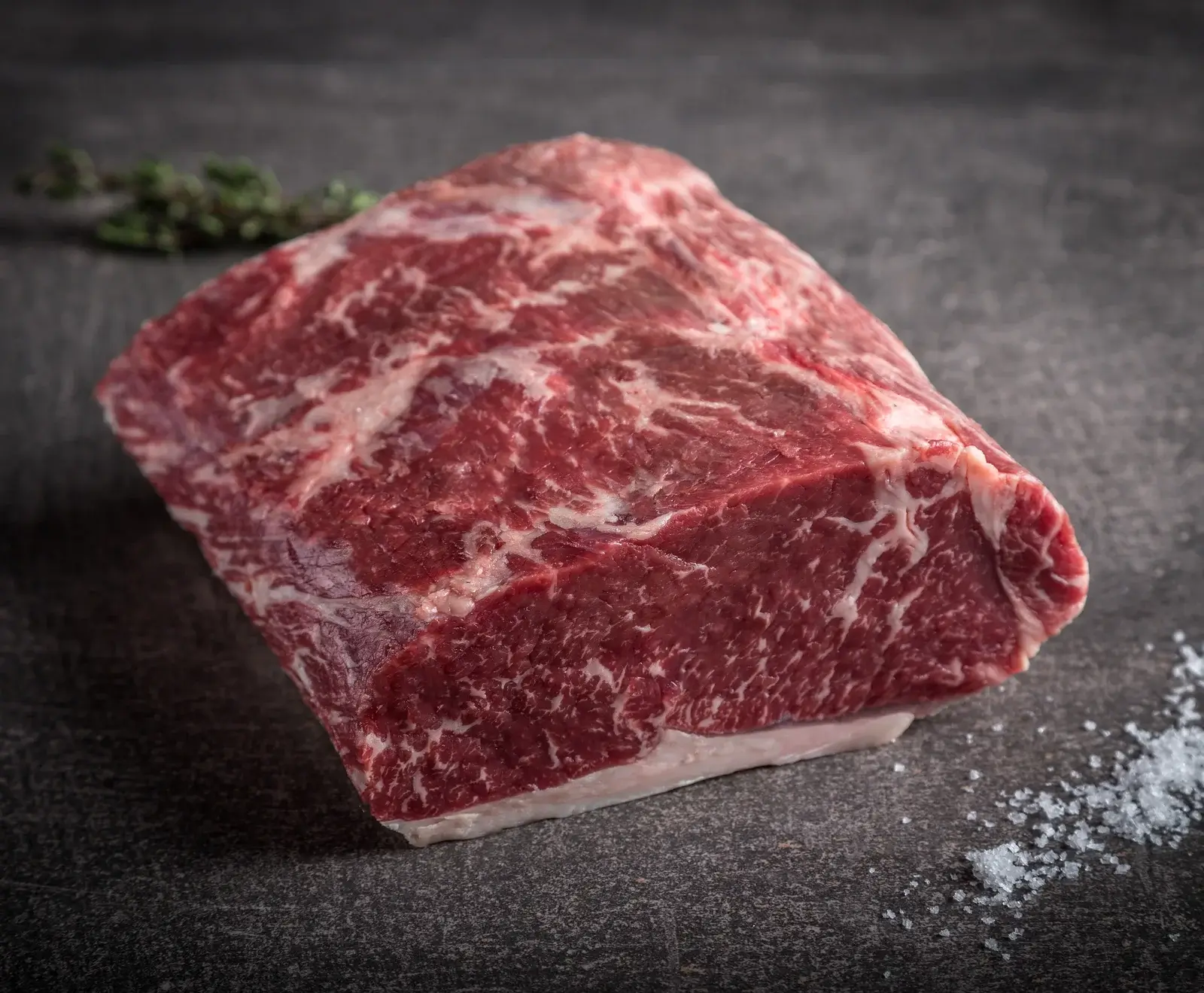 Ein Stück rohes Rindfleisch, marmoriert mit Fett, auf dunklem Hintergrund mit Salz bestreut