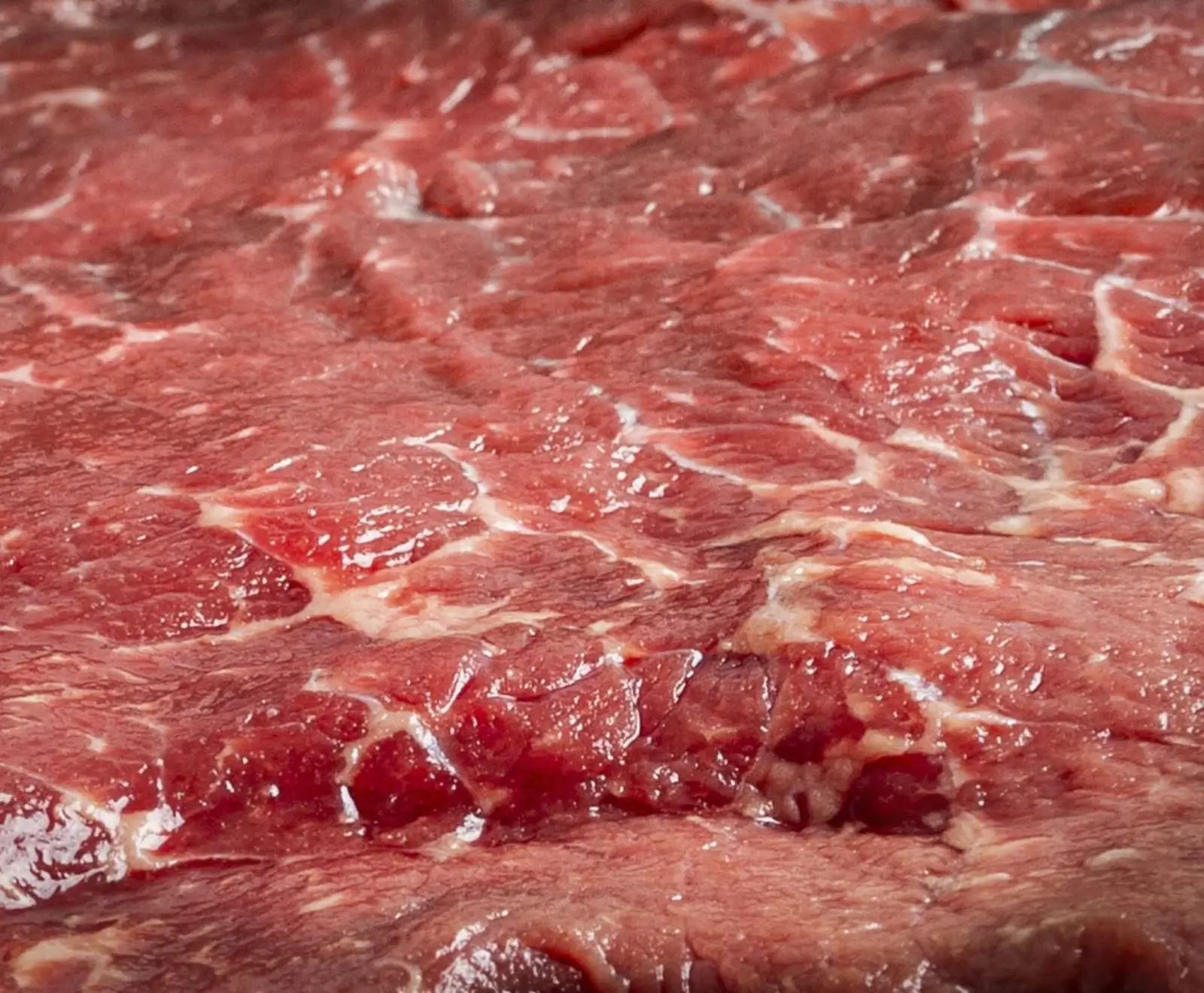 Nahaufnahme von rotem Rindfleisch mit deutlicher weißer Marmorierung und glänzender, feuchter Oberfläche, bereit zur Zubereitung.