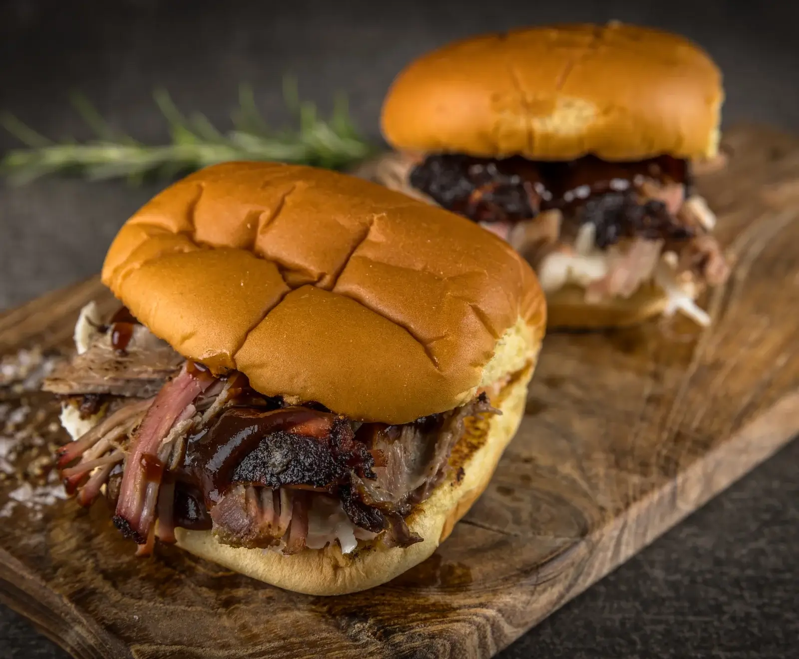 Zwei Pulled Pork Sandwiches mit Barbecue-Sauce und Zwiebeln auf einem Holzbrett