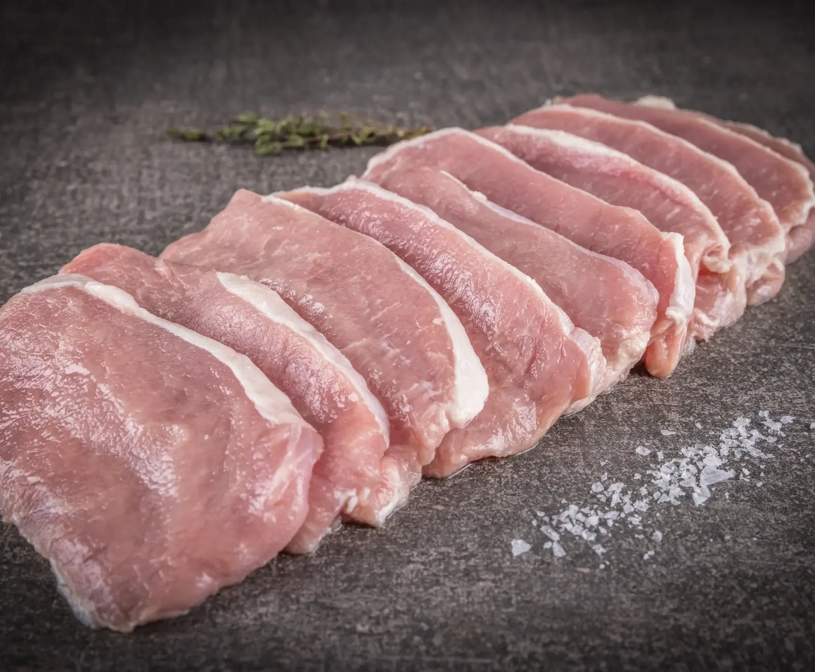 Rohes Schweinefleisch, in Scheiben geschnitten, auf einer dunklen Oberfläche mit Salz bestreut