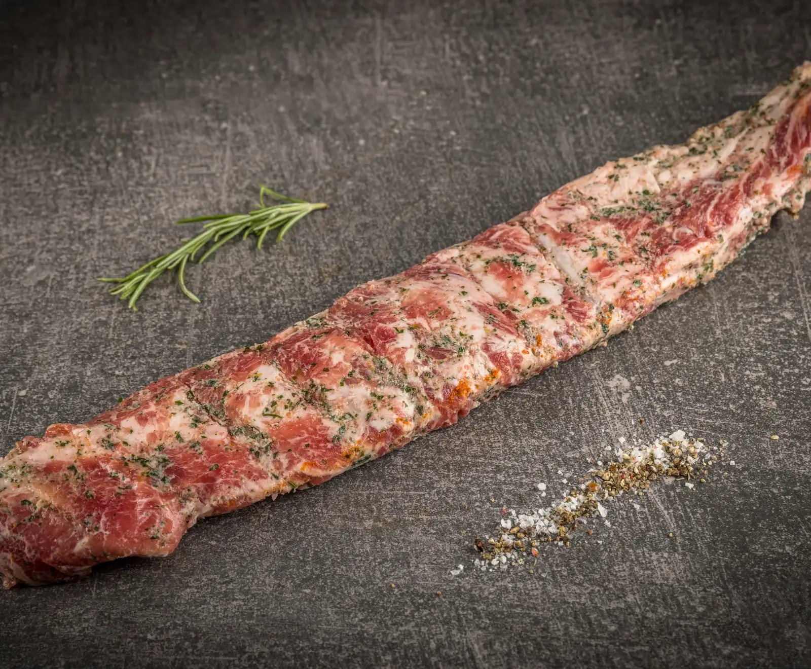 Rohes Rindersteak, mit Kräutern mariniert, auf dunklem Hintergrund mit Salz daneben.