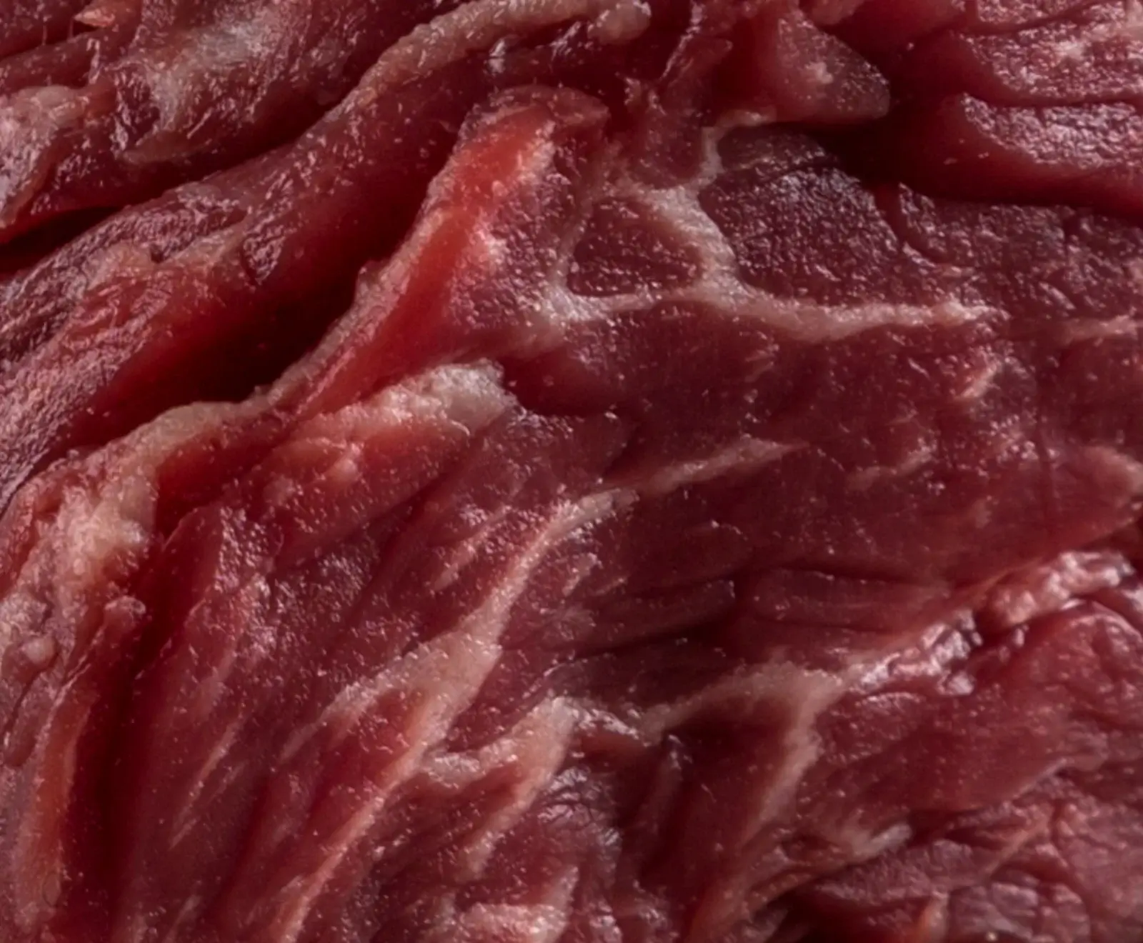 Nahaufnahme von rohem, dunkelrotem Fleisch mit deutlicher weißer Fettmarmorierung, die sich durch die Muskelfasern zieht.