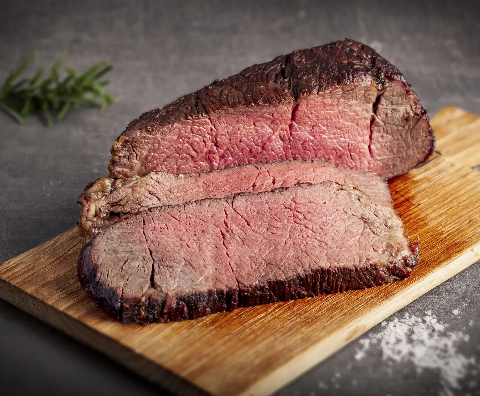 Saftiges, rosa gebratenes Steak auf Schneidebrett mit Salz und Rosmarin garniert