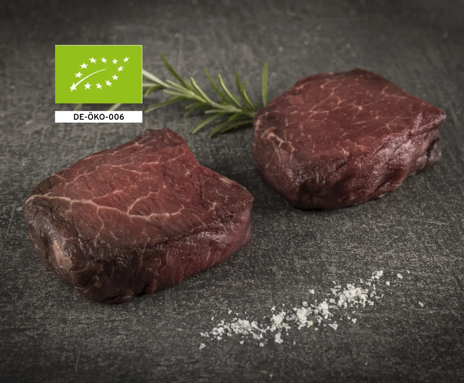 Zwei rohe Bio-Rindersteaks mit Rosmarin und Salz auf dunklem Hintergrund
