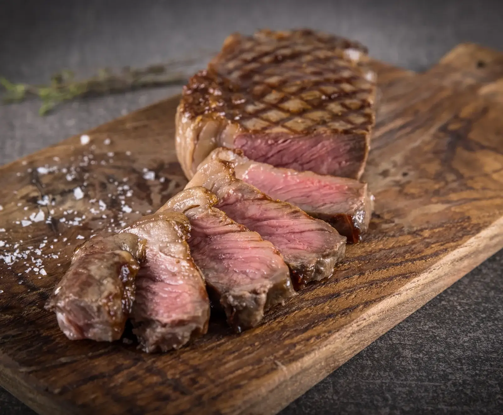 Ein perfekt gegrilltes Steak, in Scheiben geschnitten, mit rosa Kern und Grillspuren, auf einem Holzbrett mit grobem Salz bestreut.