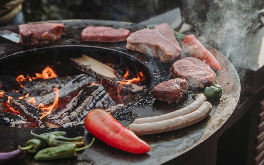 Eine Auswahl an verschiedenen Flesichcuts und ein paar leckere Beilagen auf einer Grillplatte mir Feuer