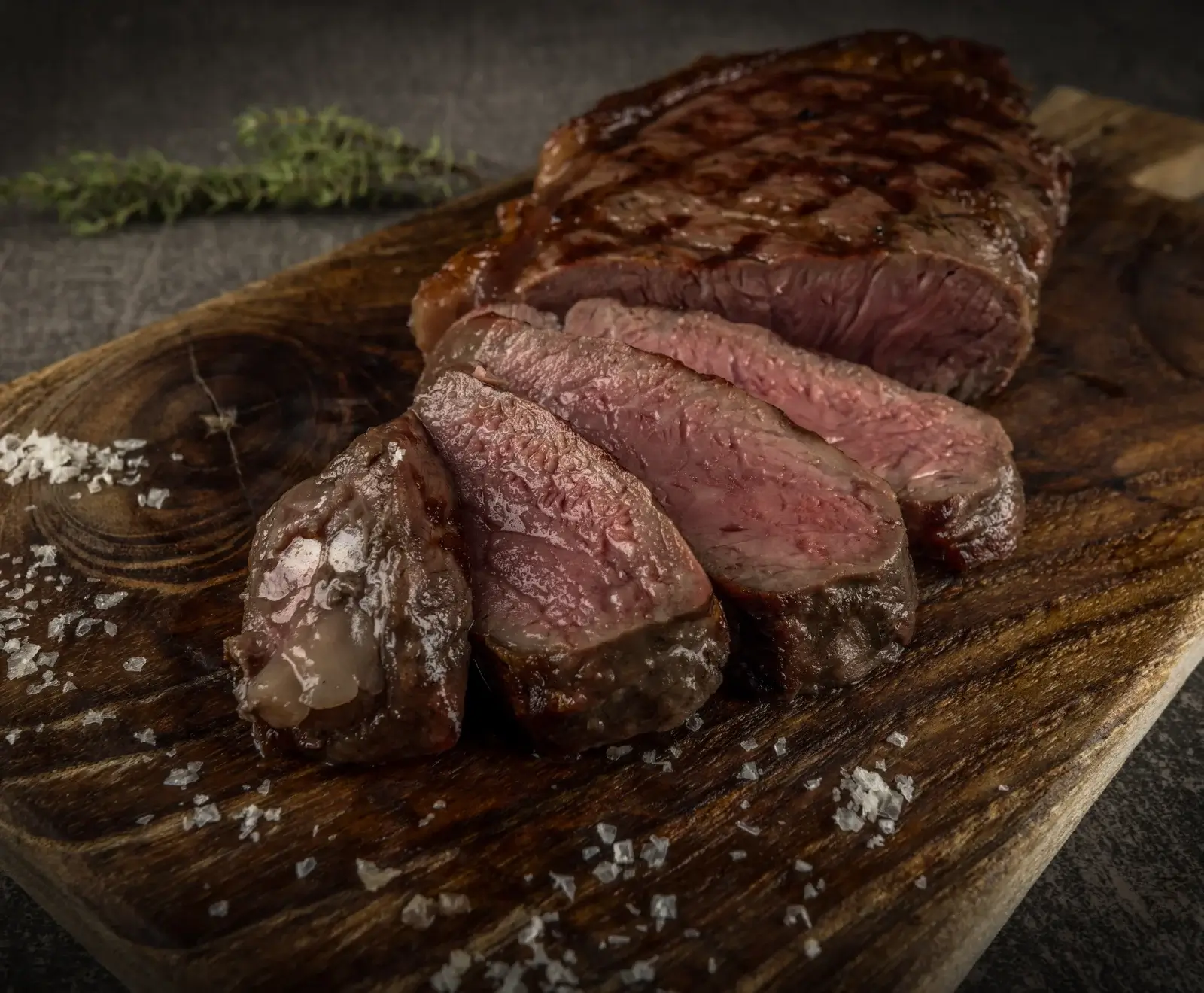Gegrilltes Rindfleischsteak mit Gewürzen auf einem hölzernen Schneidebrett, umgeben von Thymianzweigen.