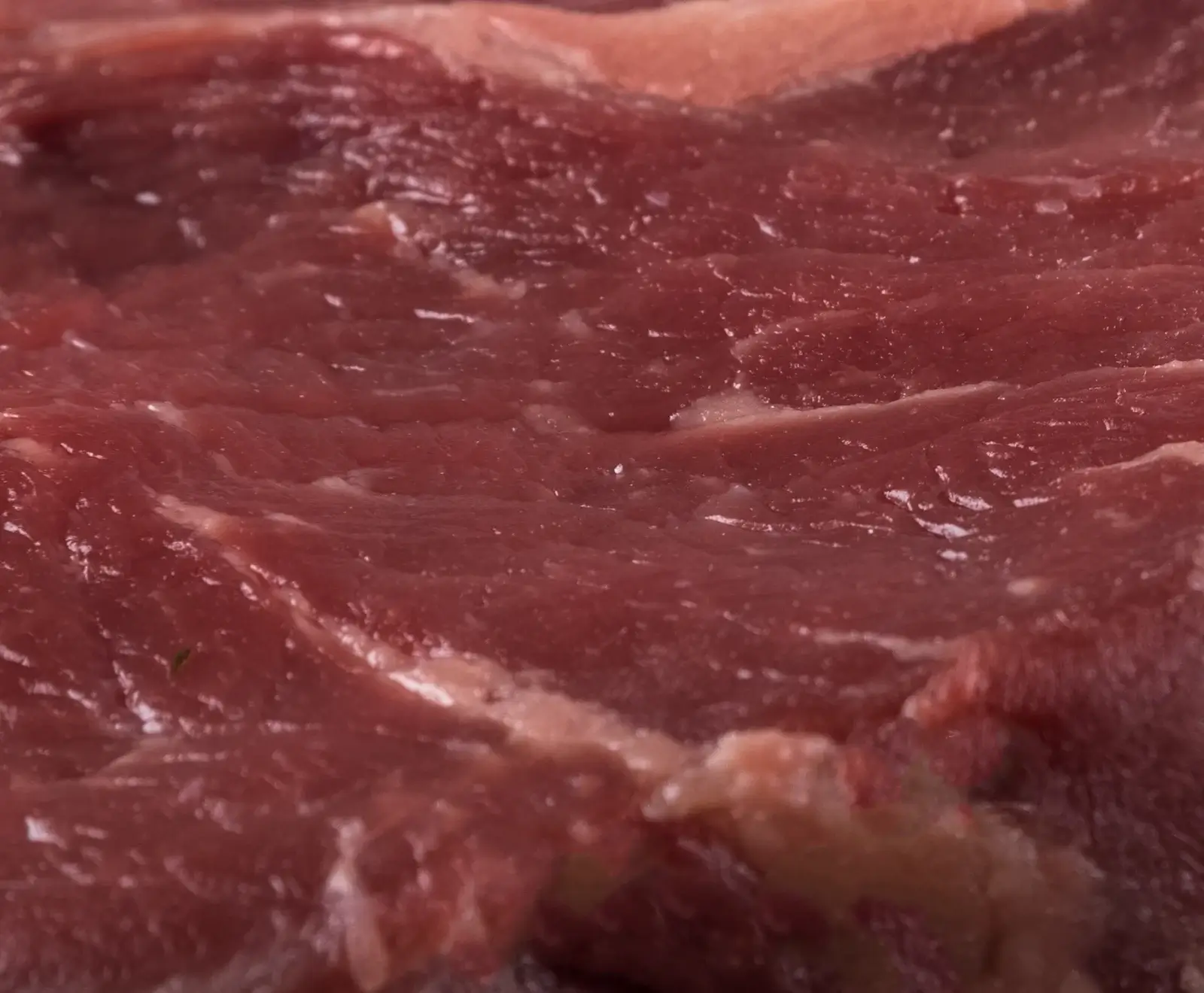 Nahaufnahme von frischem, rotem Fleisch mit sichtbaren Muskelfasern und feinen Fettstreifen. Die Oberfläche wirkt feucht und glänzend.