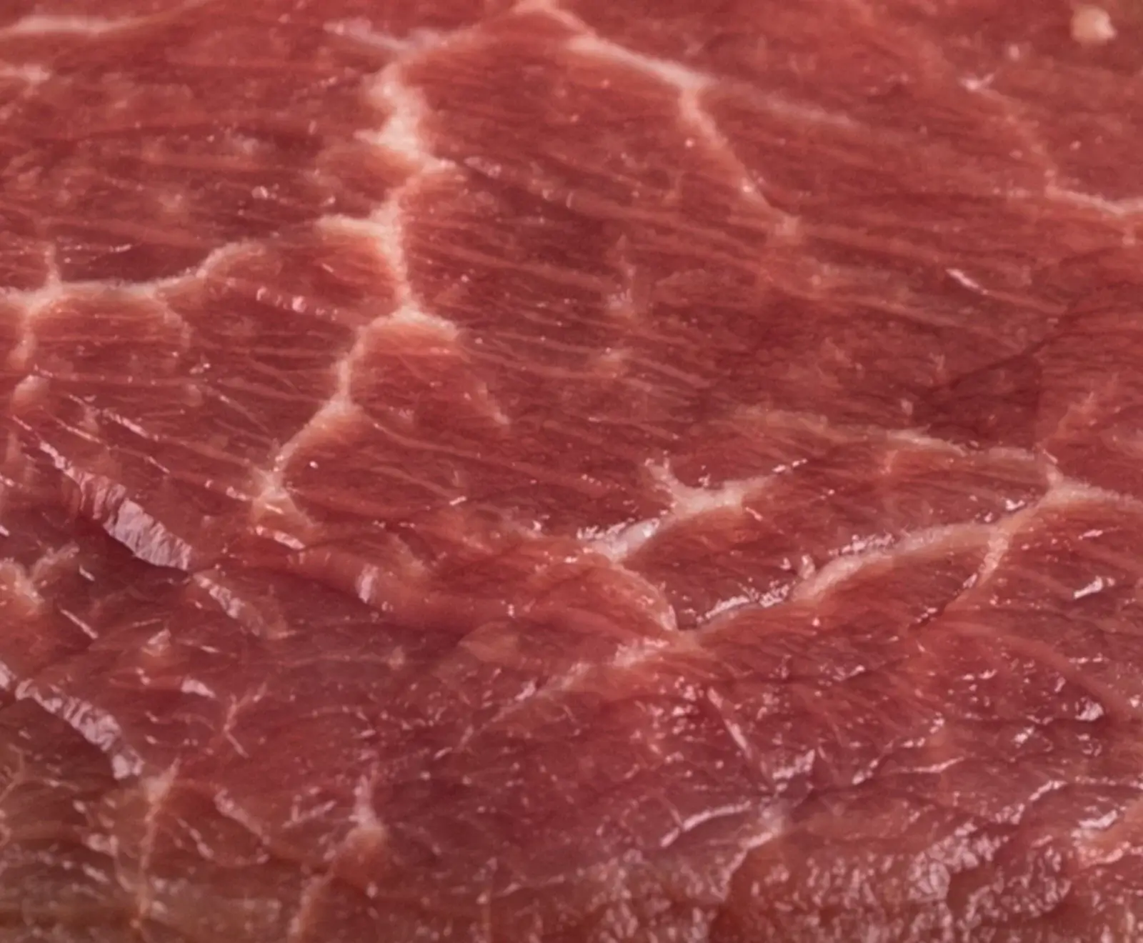 Nahaufnahme von rotem, rohem Fleisch mit sichtbaren Muskelfasern und feinen weißen Fettadern, die eine natürliche Marmorierung bilden.