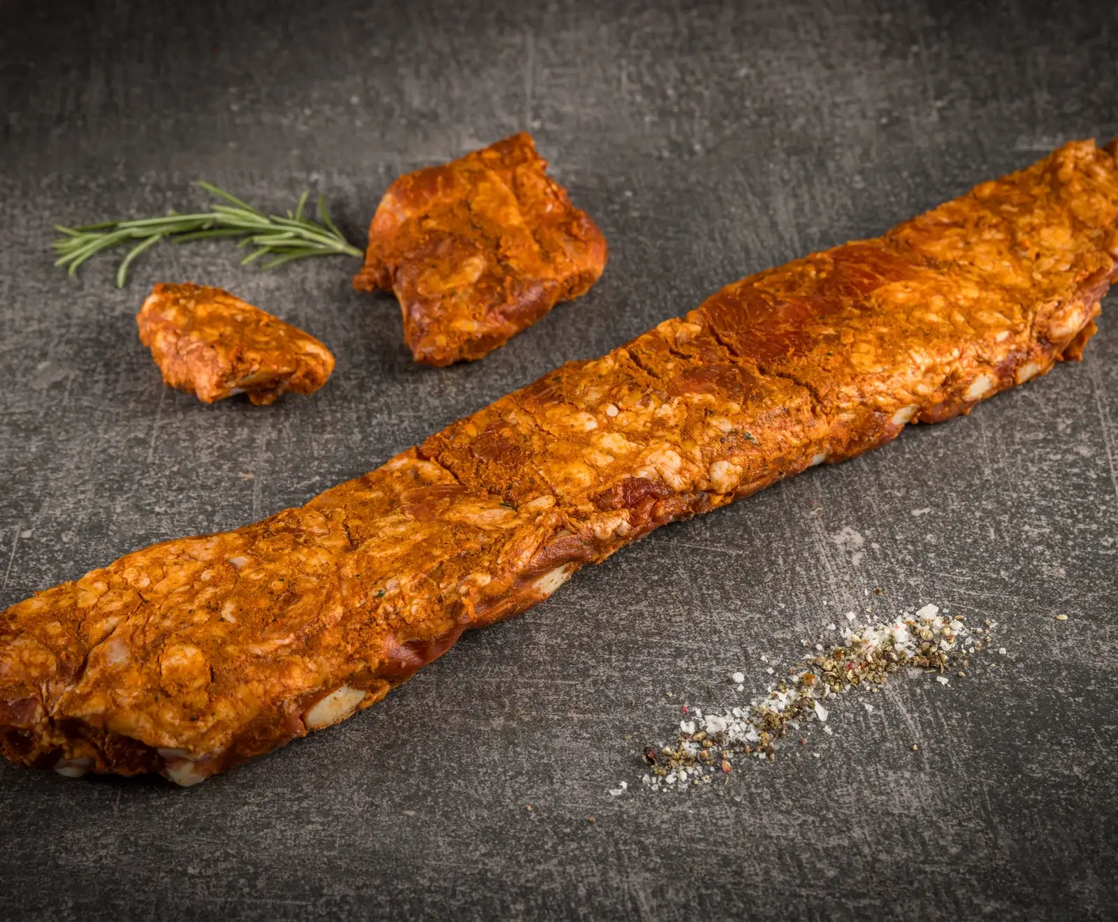 Zwei lange Scheiben Rindfleisch mit Salz und Rosmarin auf einer dunklen Schieferplatte.