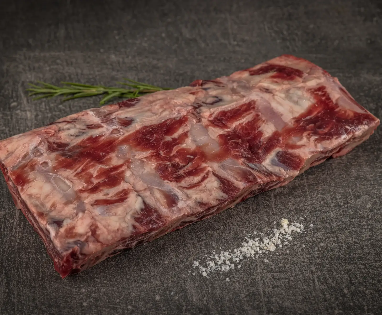 Rohe Rinderbauchlappen mit Fett und Rosmarin auf einem dunklen Hintergrund mit Salz bestreut.