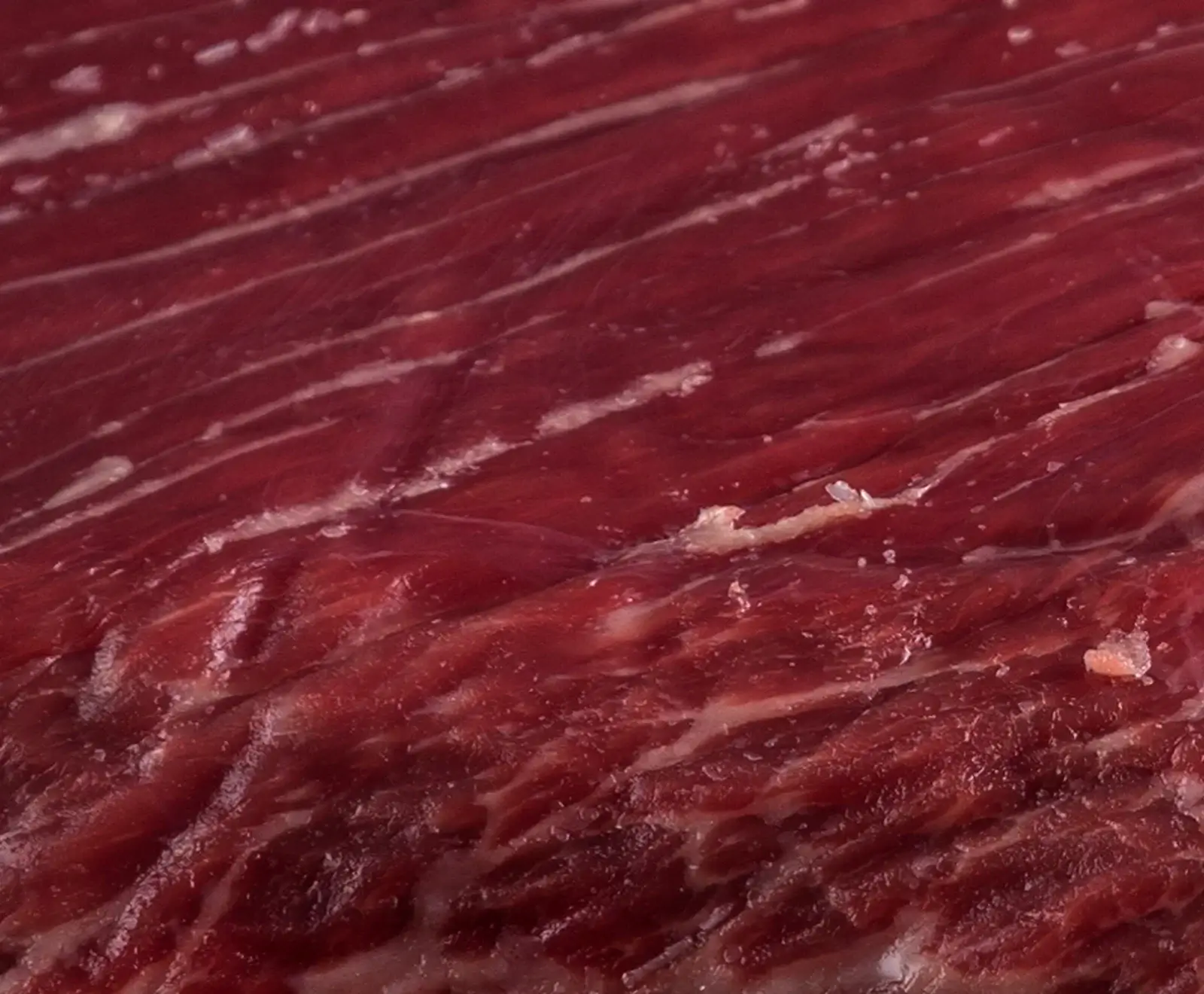 Nahaufnahme von rohem, dunkelrotem Rindfleisch mit Fettmaserung und Sehnen