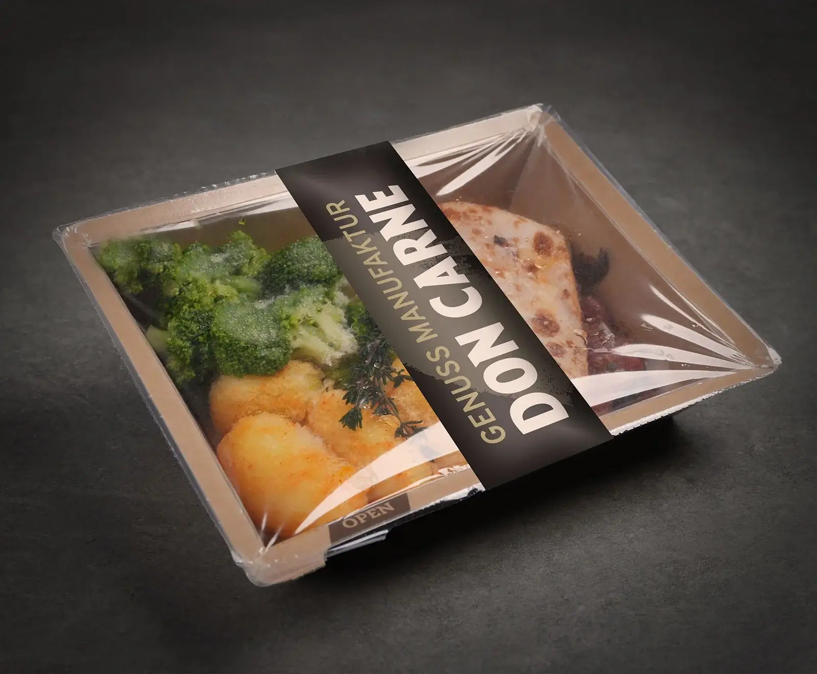 Ein verpacktes Fertiggericht von "DON CARNE" mit Brokkoli, goldbraunen Kartoffeln und einem Stück Fleisch in einer transparenten Schale mit schwarzem Etikett auf dunklem Hintergrund.