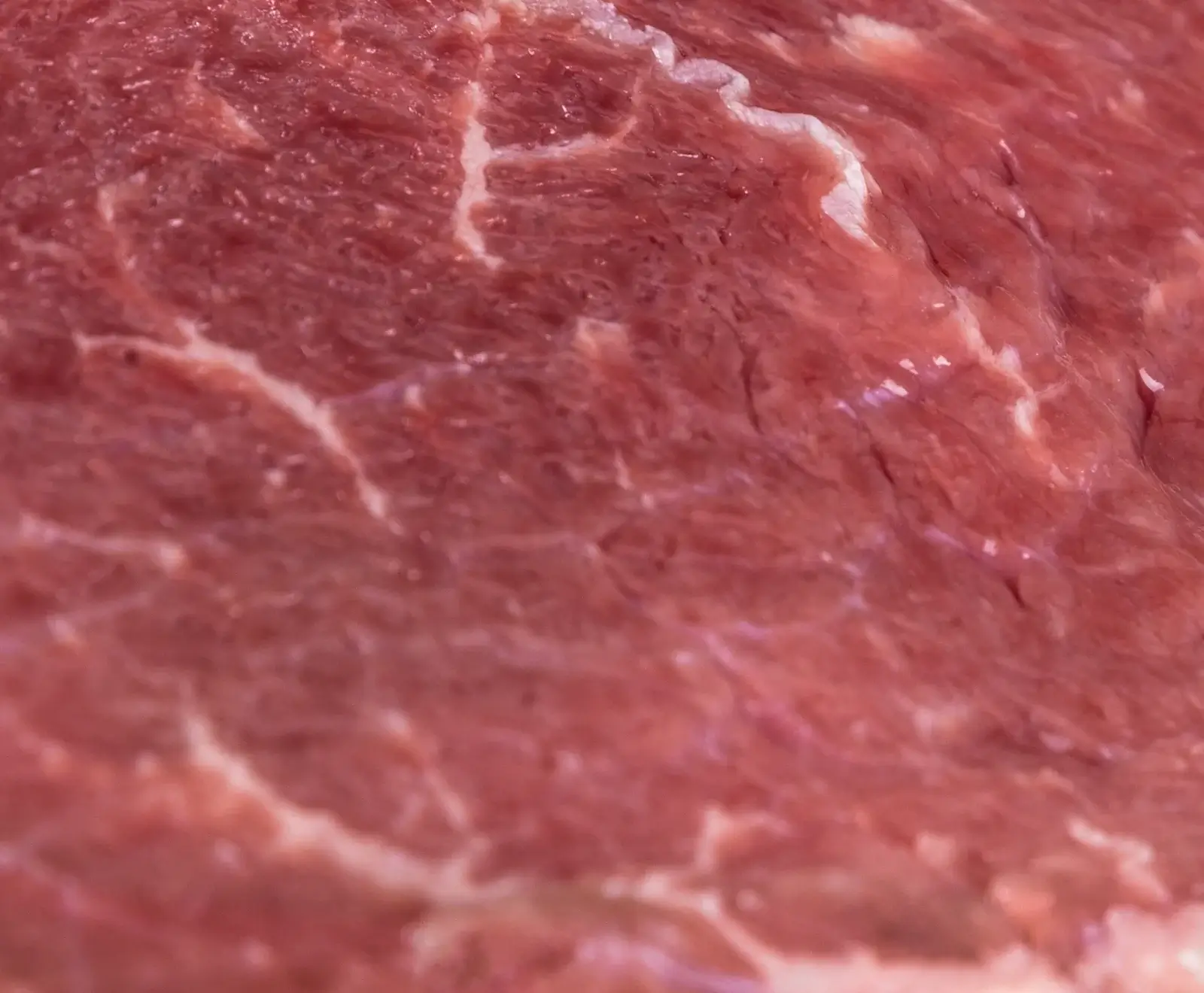 Detailaufnahme von frischem, rotem Fleisch mit feiner Marmorierung und sichtbaren Fasern.