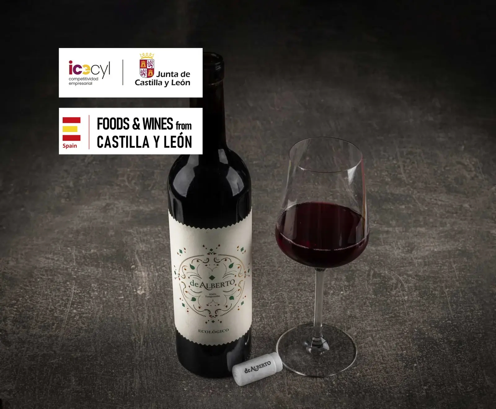 Eine Flasche Rotwein "de Alberto" (ökologisch, 100% Tempranillo) und ein gefülltes Weinglas auf dunklem Hintergrund. Oben links Logos von "Junta de Castilla y León" und "Foods & Wines from Castilla y León".