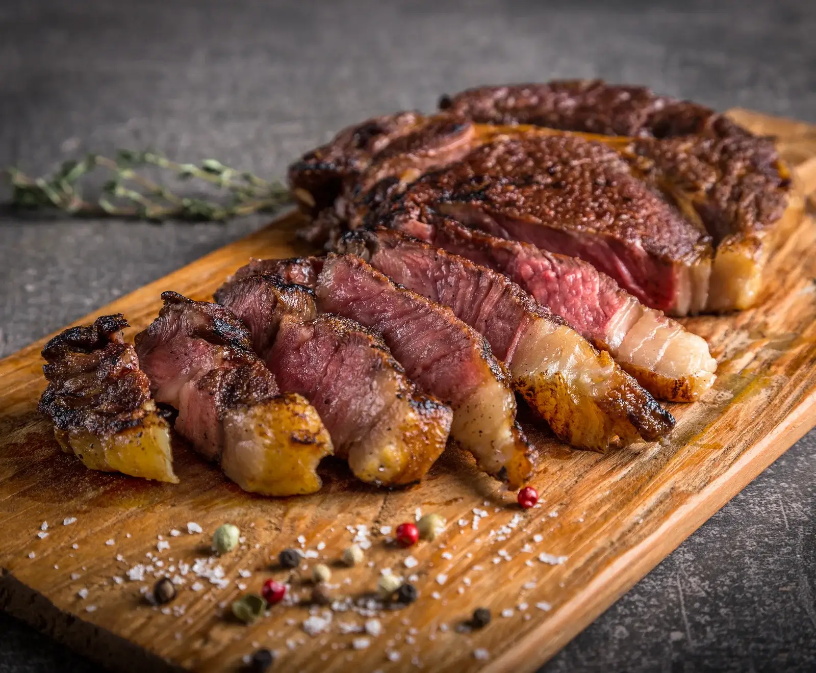 Gegrilltes Rindfleisch in Scheiben geschnitten auf einem Holzbrett, garniert mit Kräutern und Gewürzen