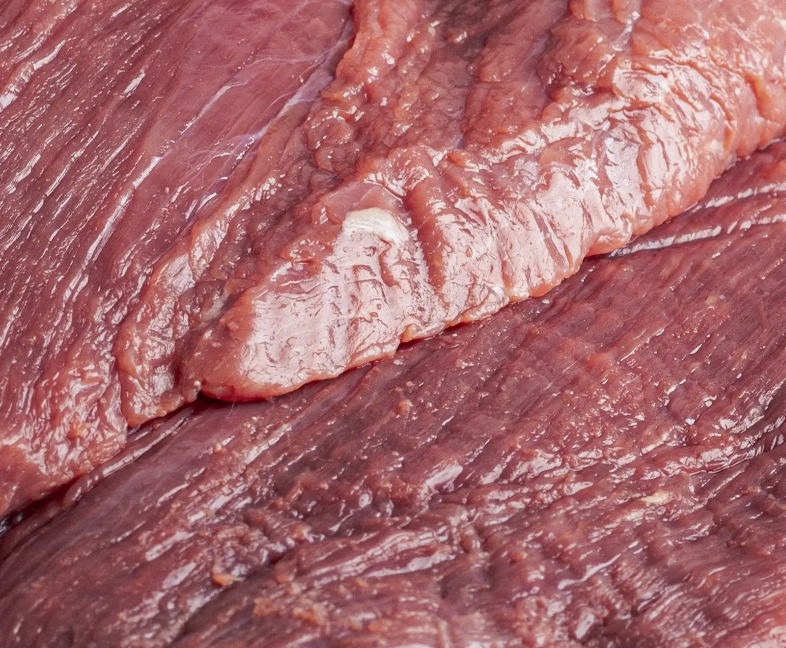 Nahaufnahme von rohem Rindfleisch mit Fettadern auf einer dunklen Oberfläche