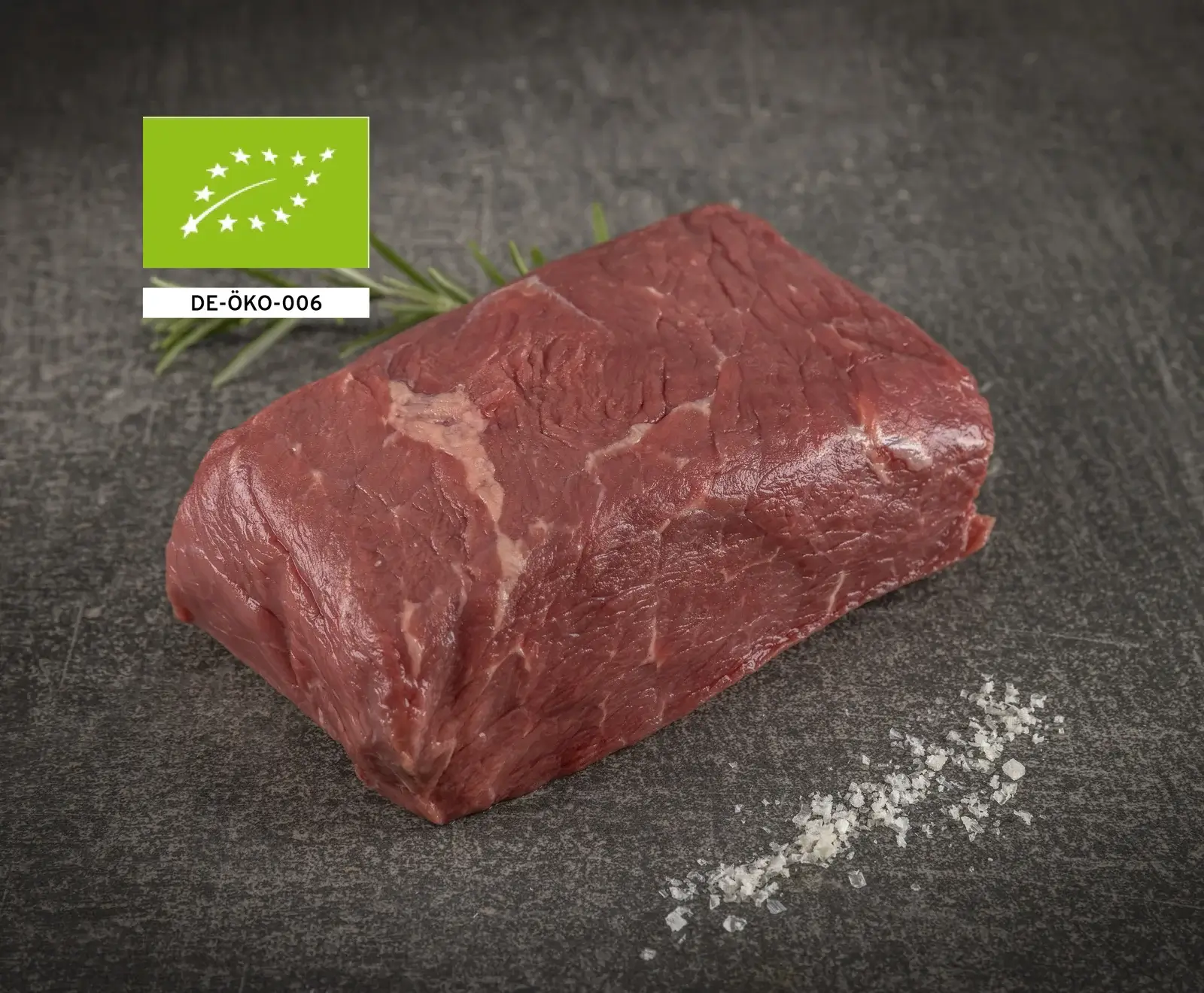 Rohes Bio-Rindfleischstück mit EU-Bio-Siegel und Artikelnummer auf dunklem Hintergrund mit Salz