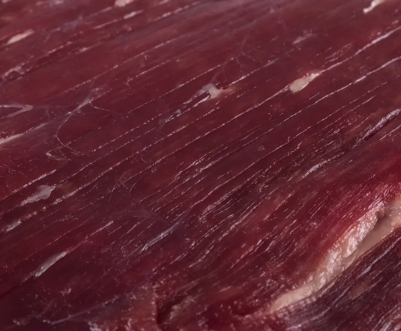 Nahaufnahme von dunkelrotem, rohem Fleisch mit deutlich sichtbaren, diagonal verlaufenden Muskelfasern und einigen hellen Bindegewebsstreifen.